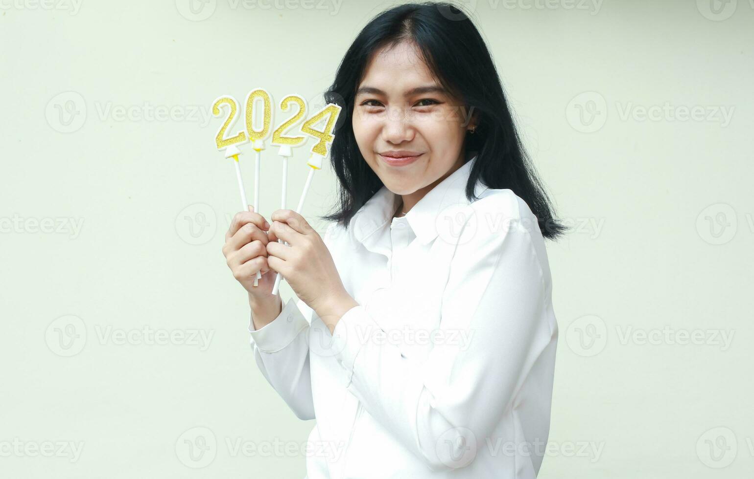 retrato de contento asiático joven mujer participación dorado velas número 2024 a celebrar nuevo años víspera vestir formal blanco traje mirando a cámara aislado terminado blanco antecedentes foto