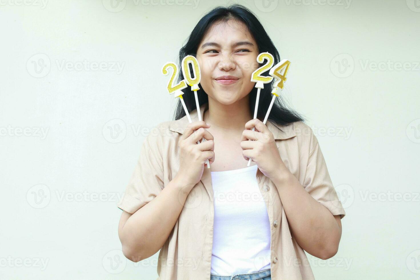 happy succesful asian young woman celebrating 2024 new years eve by holding gloden figure candles and flirting looking aside wear brown casual outer isolated over white background photo