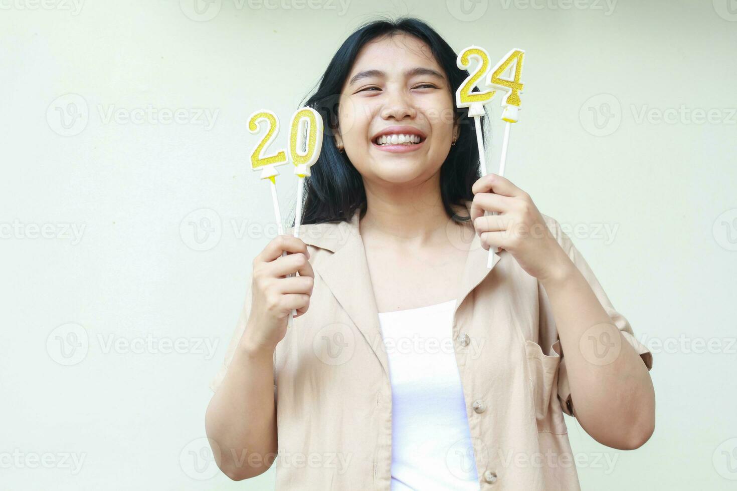 juguetón asiático joven mujer riendo y mirando aparte con participación 2024 oro velas número a celebrar nuevo años víspera vistiendo casual marrón ropa aislado en blanco antecedentes foto