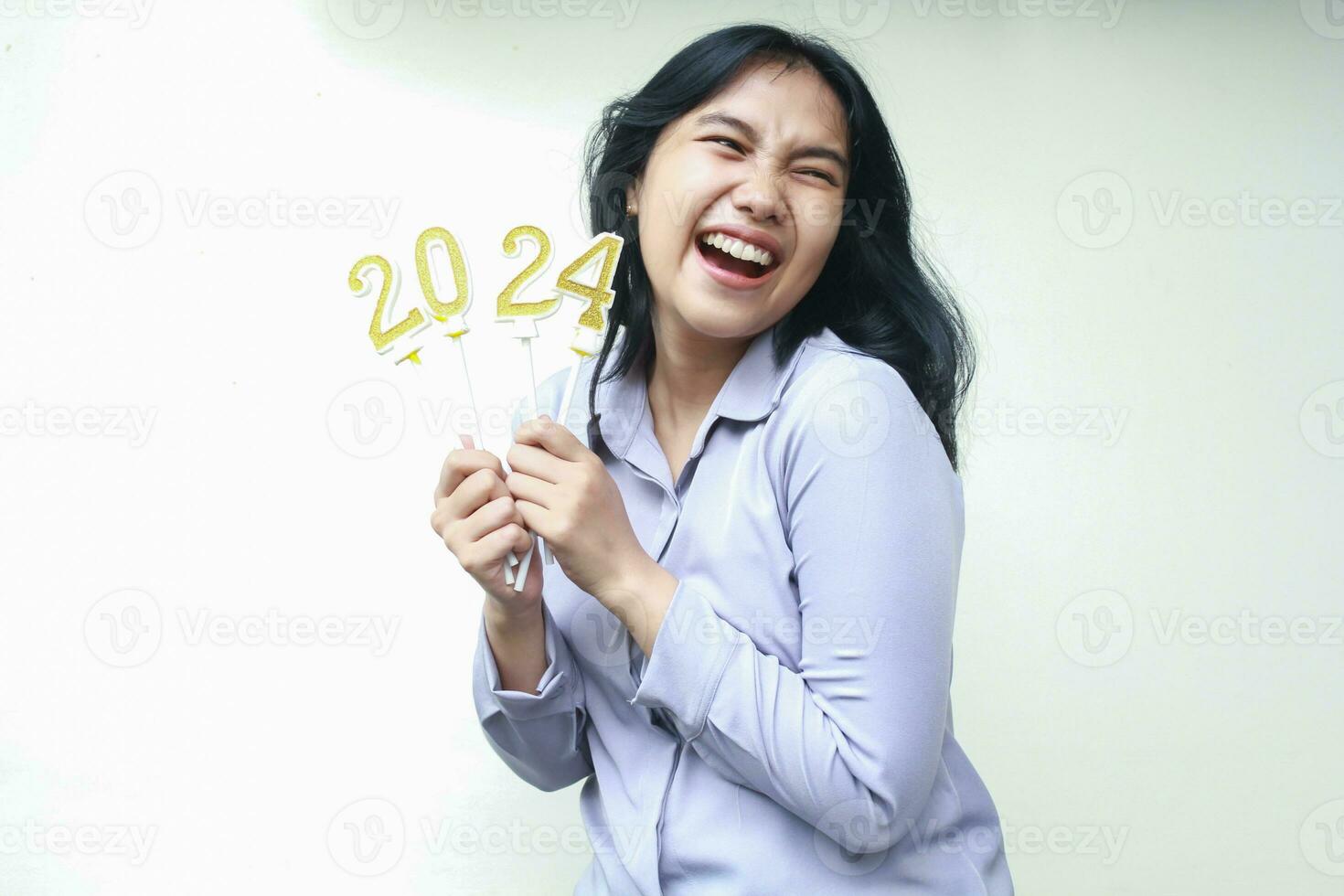 excited asian young business woman laughing and looking away with open mouth while lifting 2024 figure candle hold on hand wearing grey formal suit, isolated, female coworker celebrating new year eve photo