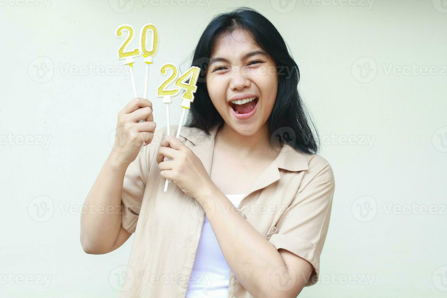 excited asian young woman hipster wearing trendy brown outer shouting to camera with raising 2024 figure candles hold on hand to announce new years eve changing calendar, isolated o white background photo