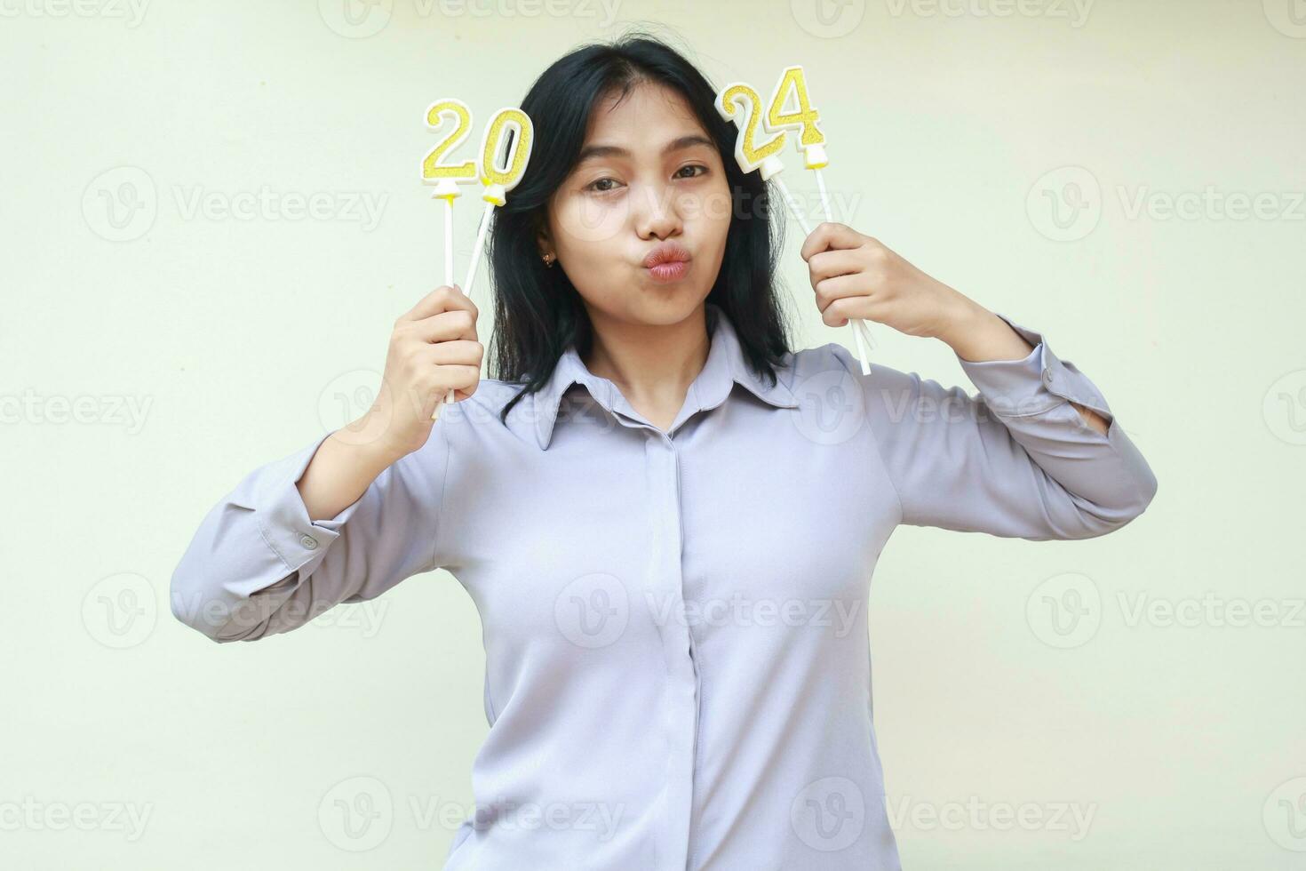 happy asian young woman holding 2024 golden number candles and looking to camera with duck face wear grey formal suit. smiling indonesian female celebrating new years eve isolated photo