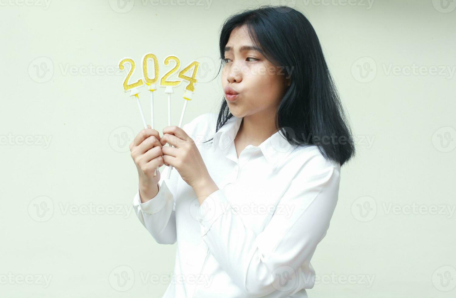 thoughtful asian young woman holding 2024 figure candle with curiosity and looking aside to number 24 wearing white formal shirt, isolated photo