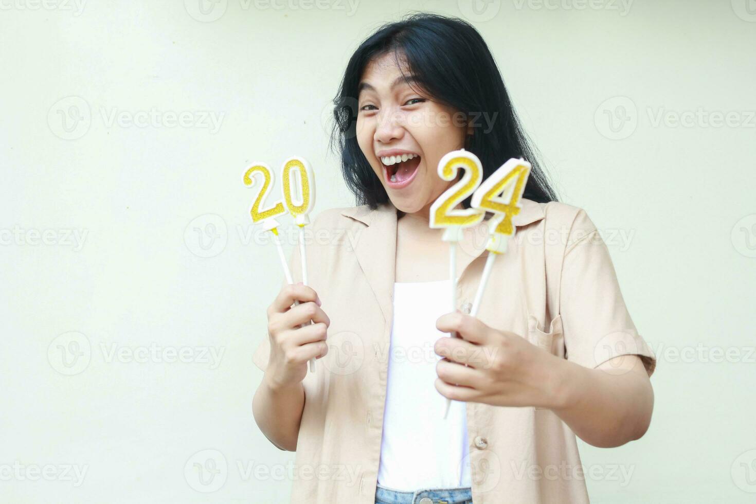 happy young woman asian screaming with holding 2024 number candle looking at camera, beautiful female hipster wearing stylish brown outer, isolated on white, new years eve concept photo