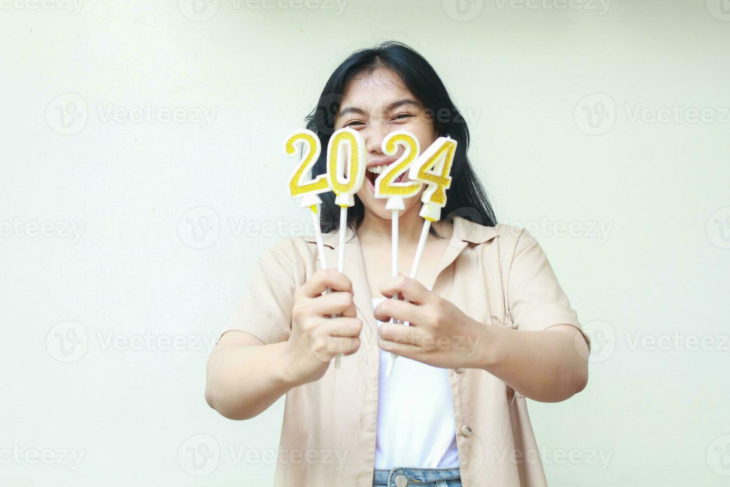 amazed young woman asiah hipster shouting with lifting arm show 2024 number candle hold on hand wearing fashionable brown outer, isolated over white background photo