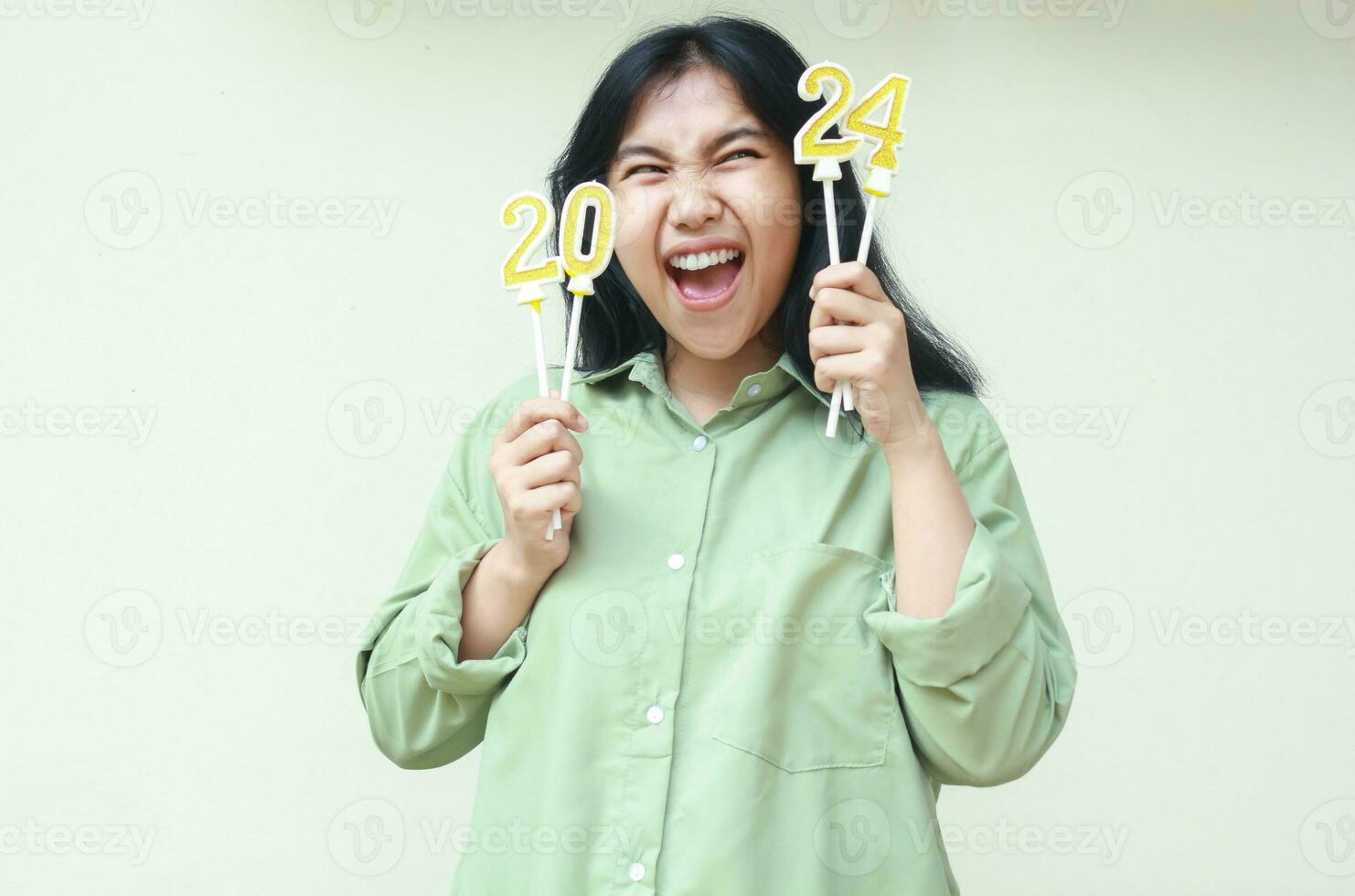 sorprendido asiático joven mujer gritos mientras mirando arriba y aparte a número 24 de 2024 número vela, hembra elegante hipster vestir verde casual terminado Talla camisa, aislado en blanco foto