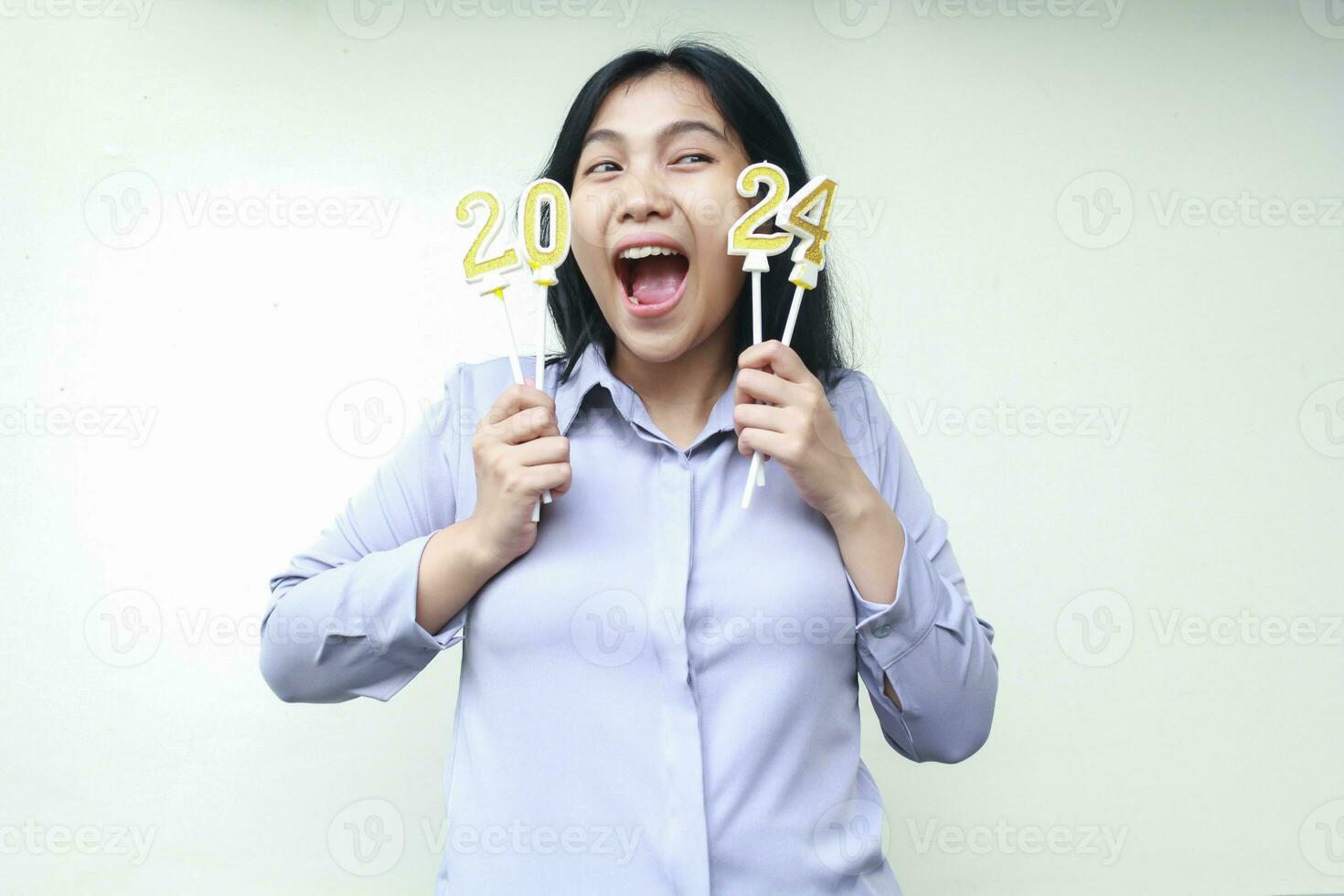 conmocionado asiático joven mujer vestir gris formal traje gritando con participación 2024 número vela elevado Entre su rostro, mirando lejos, aislado terminado blanco antecedentes foto