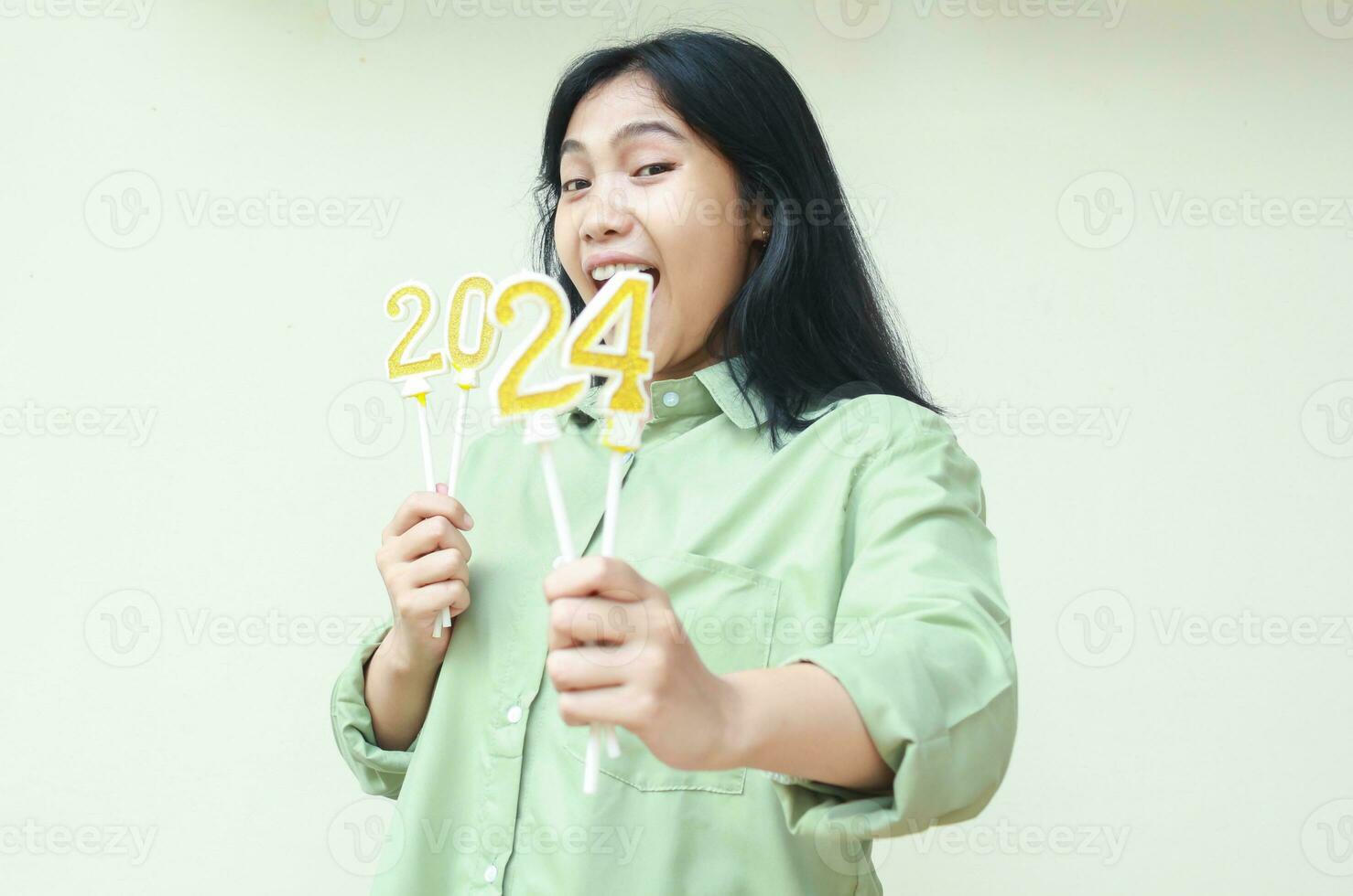 shocked asian young woman raising arm with number 24 of 2024 number candles holding on hand, female hipster wearing green casual over size shirt, isolated on white photo