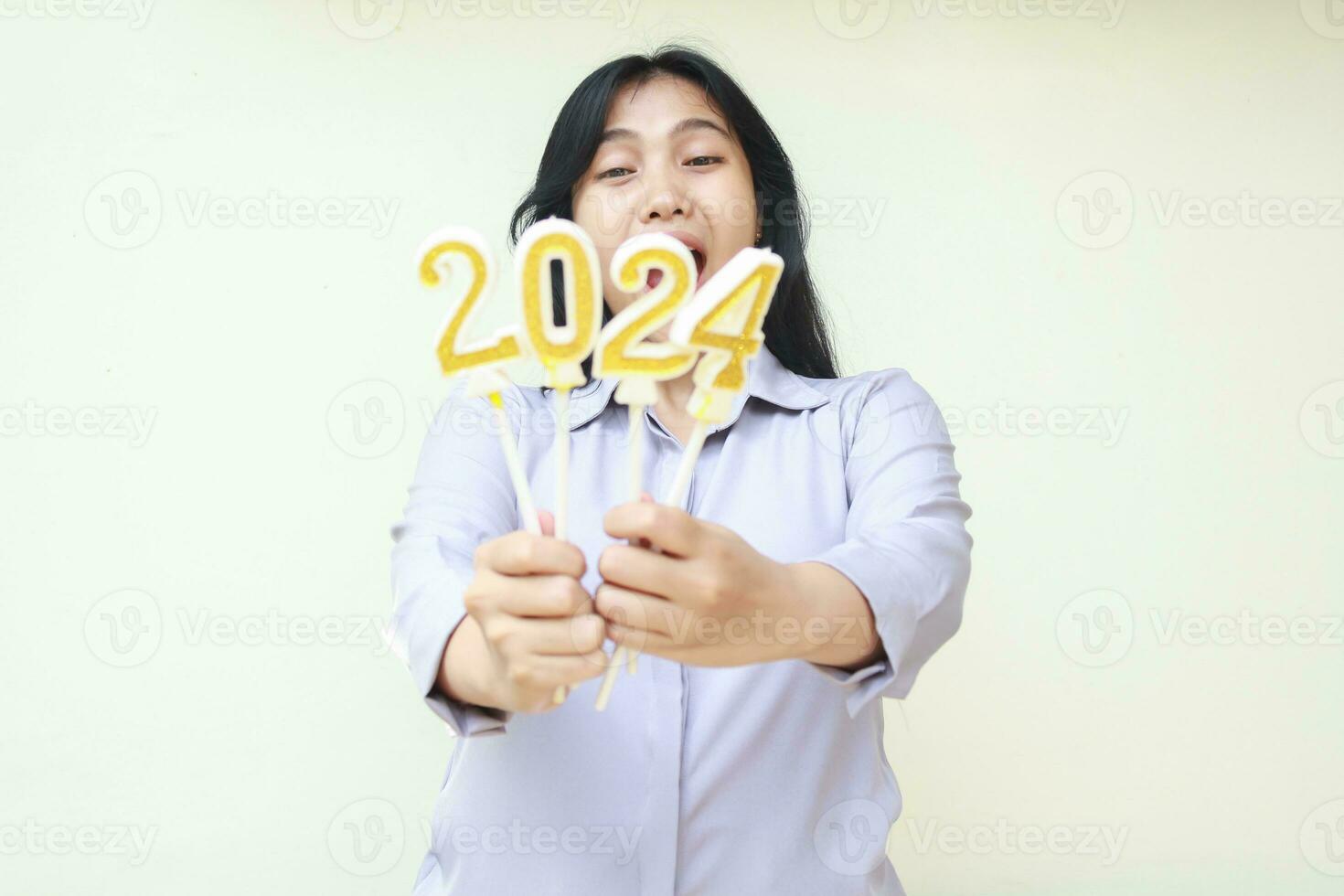 conmocionado asiático joven mujer aturdido con abierto boca mirando a 2024 número vela sostener en mano demostración a cámara, emocionado hembra vistiendo gris camisa formal, aislado en blanco foto