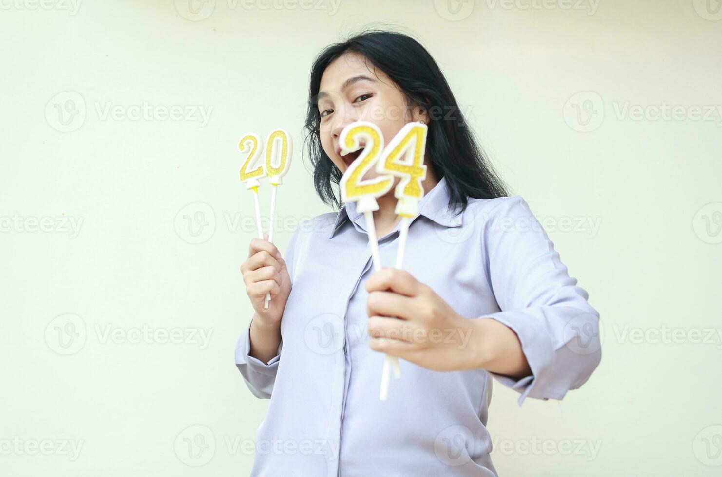 asombrado joven negocio mujer asiático gritando con demostración número 24 de 2024 número vela sostener en mano, hermosa hembra vistiendo gris formal camisa, aislado, mirando a cámara, nuevo año víspera concepto foto