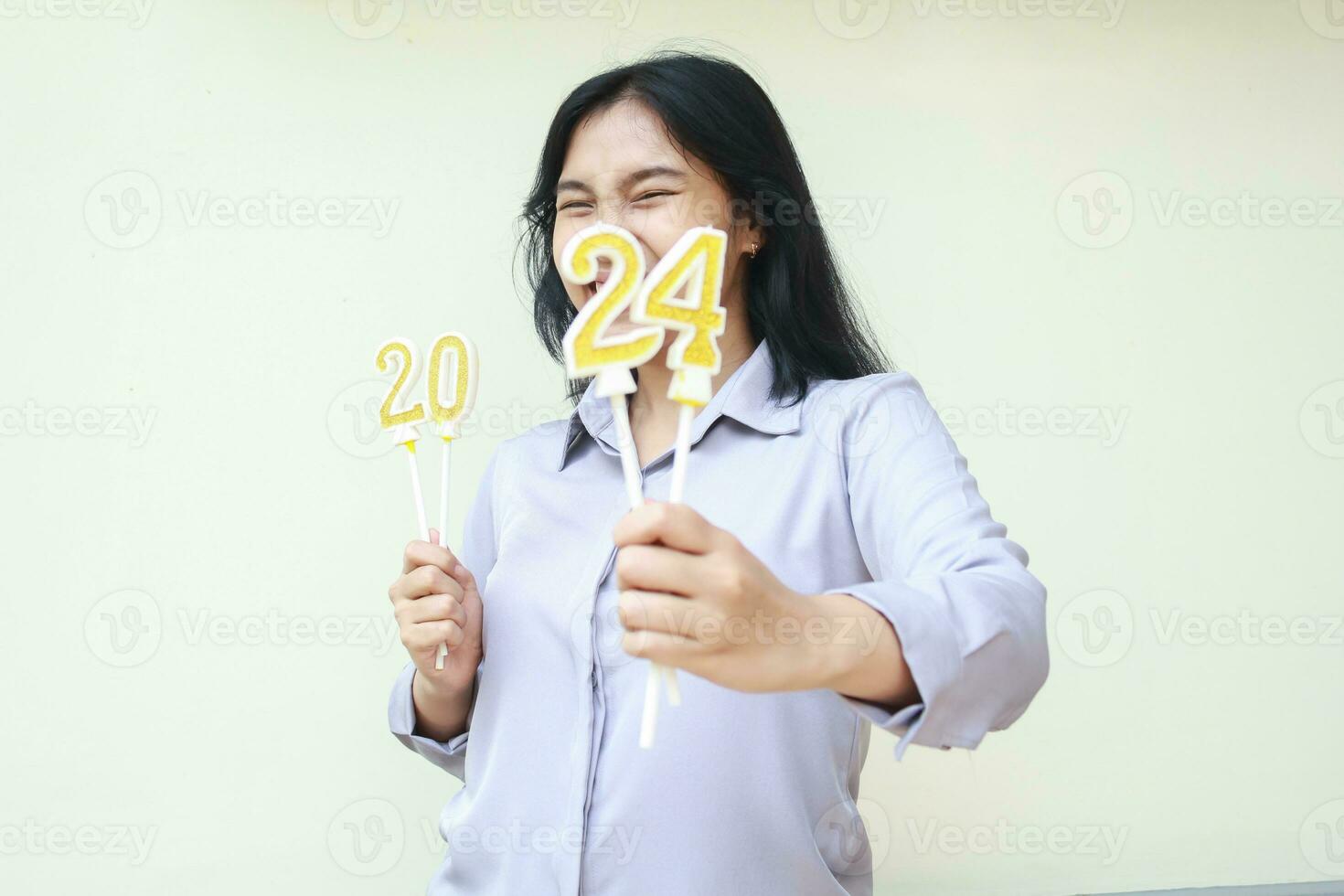 excited asian young business woman wear grey formal suit showing number 24 of 2024 number candle hold on hand, new years eve concept, looking to camera, isolated photo