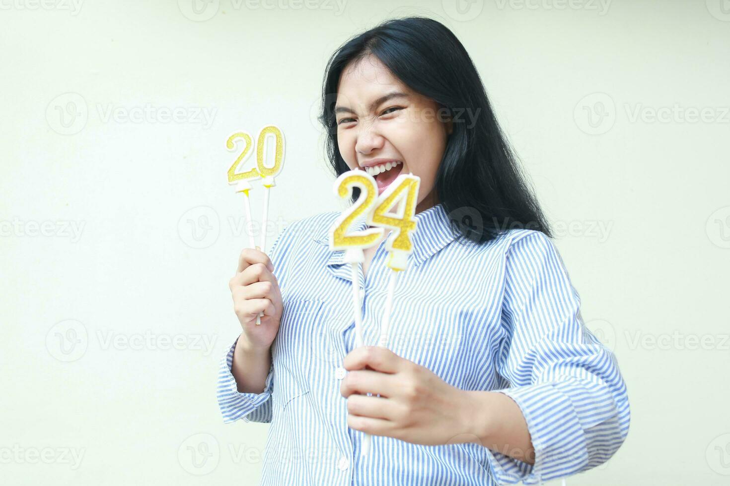 excited asian young business woman screaming while holding 2024 number candle wearing blue stripes shirt casual, isolated over white background, female coworker celebrate new years eve photo