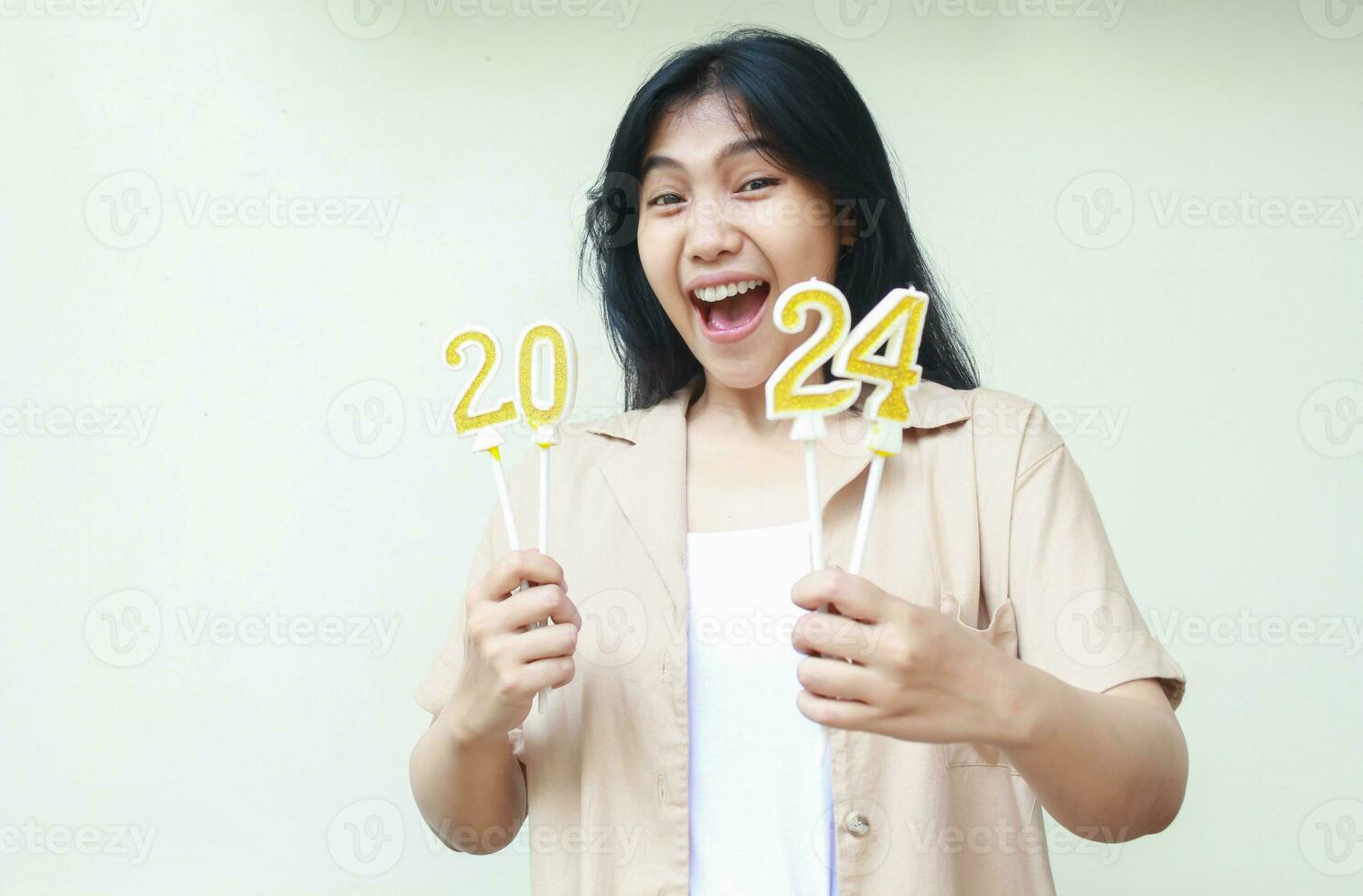 amazed young woman asian screaming to camera with holding 2024 number candles, female hipster wearing stylish brown outer for new years eve celebration, isolated on white, looking at camera photo