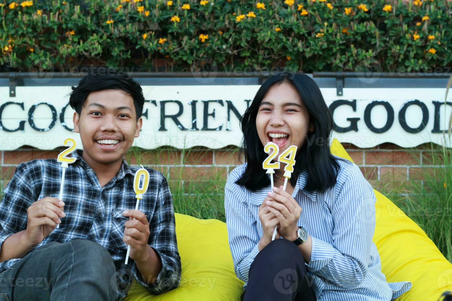 contento asiático Pareja adolescente participación número 20 24 dorado vela y sentado en amarillo frijol bolso en casa patio trasero, Mira a cámara foto