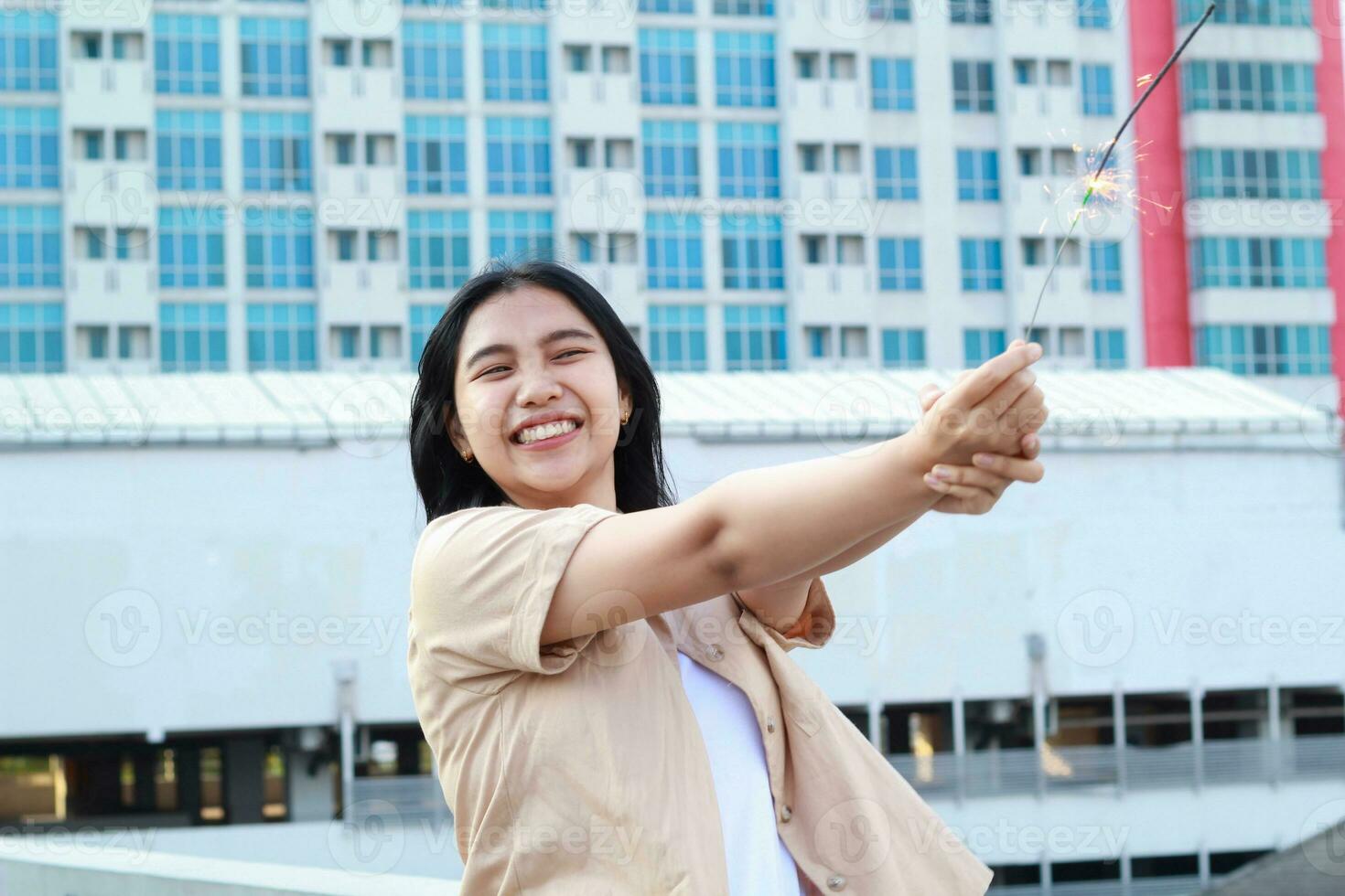 beautiful asian young woman holding sparklers firework and laughing in new year eve celebration standing in roof top outdoor with urban building background photo