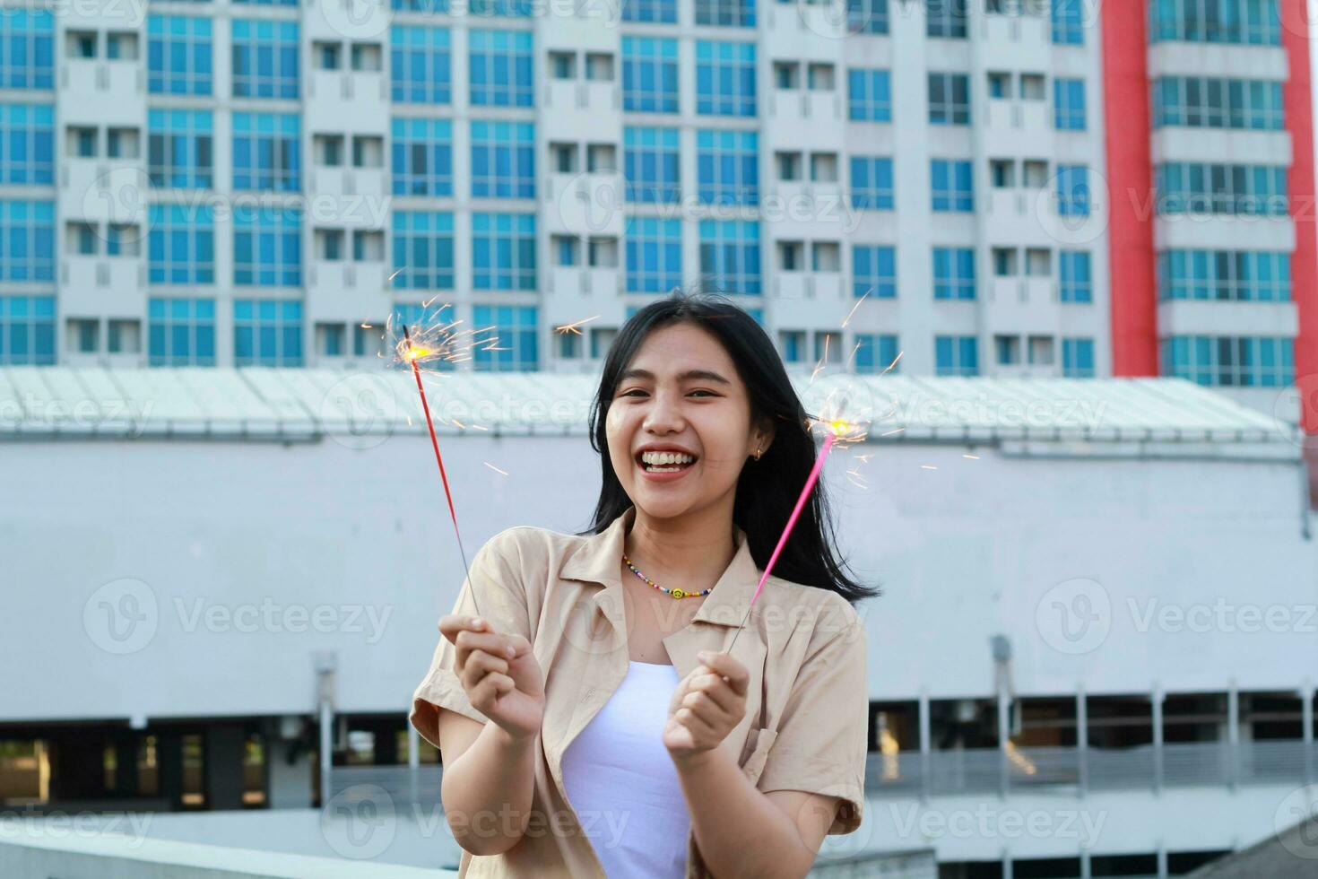 excited asian young woman holding sparkler to celebrating new year eve in rooftop apartment with city building background photo