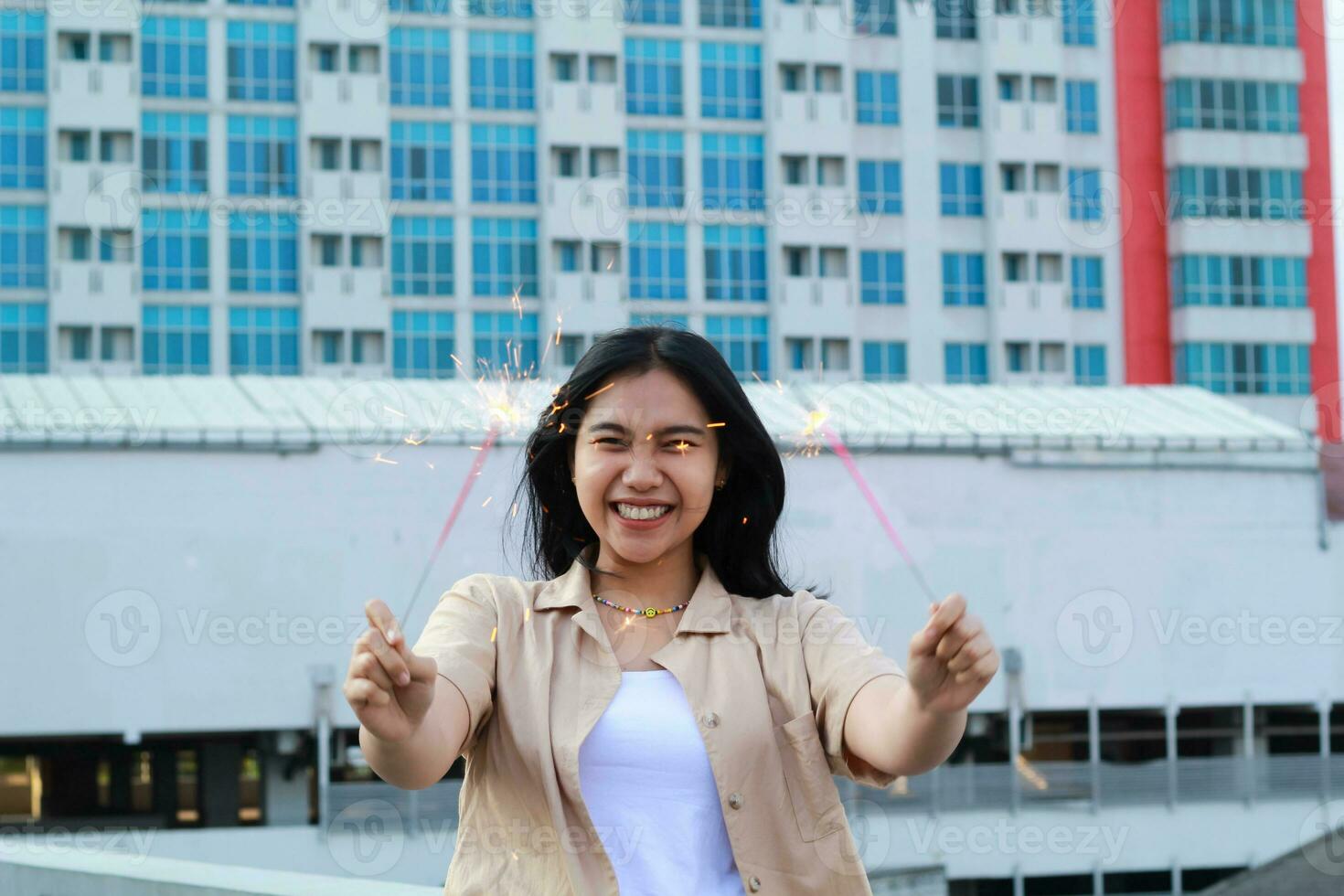 excited asian young woman holding sparkler to celebrating new year eve in rooftop apartment with city building background photo