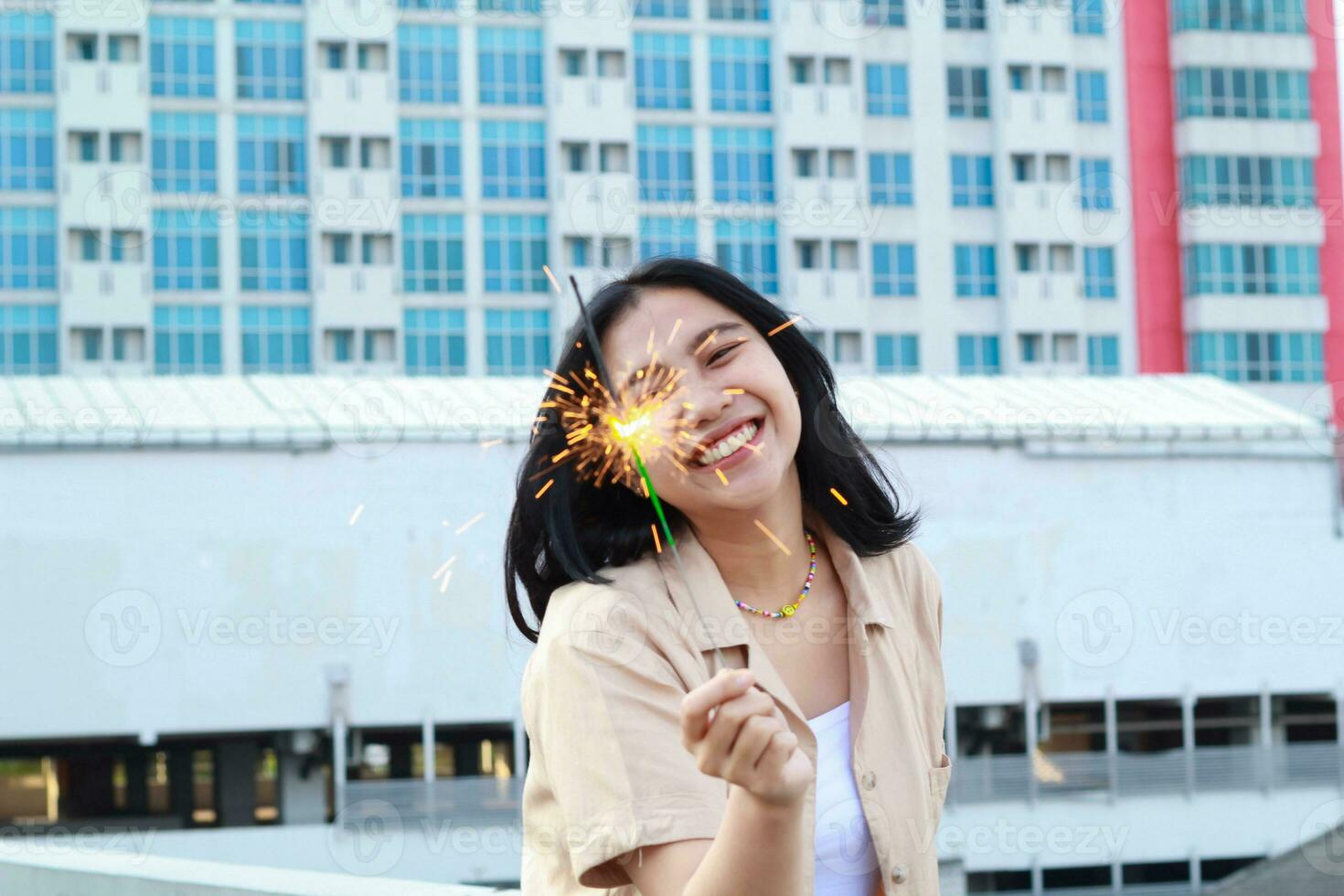 happy asian young woman holding sparklers celebrate new year eve in outdoor roof top with city building background photo