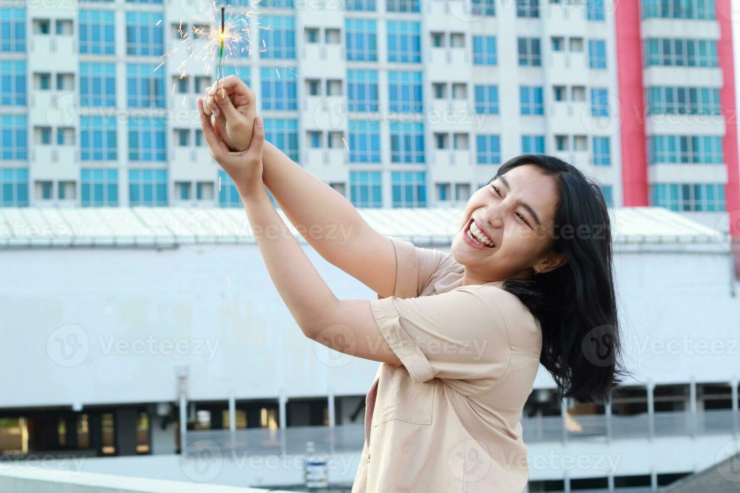 happy asian young woman holding sparklers celebrate new year eve in outdoor roof top with city building background photo