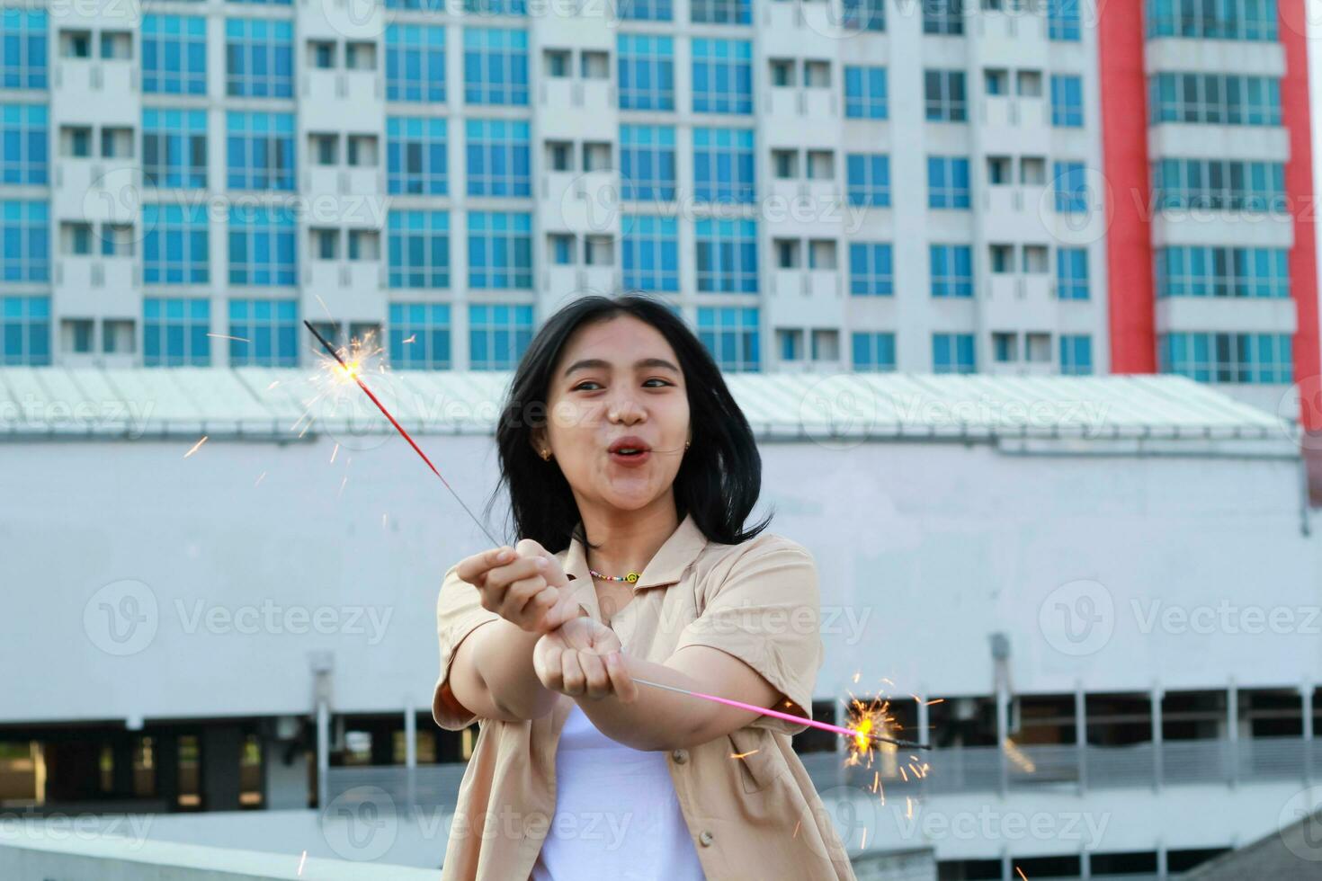 excited asian young woman holding sparkler to celebrating new year eve in rooftop apartment with city building background photo