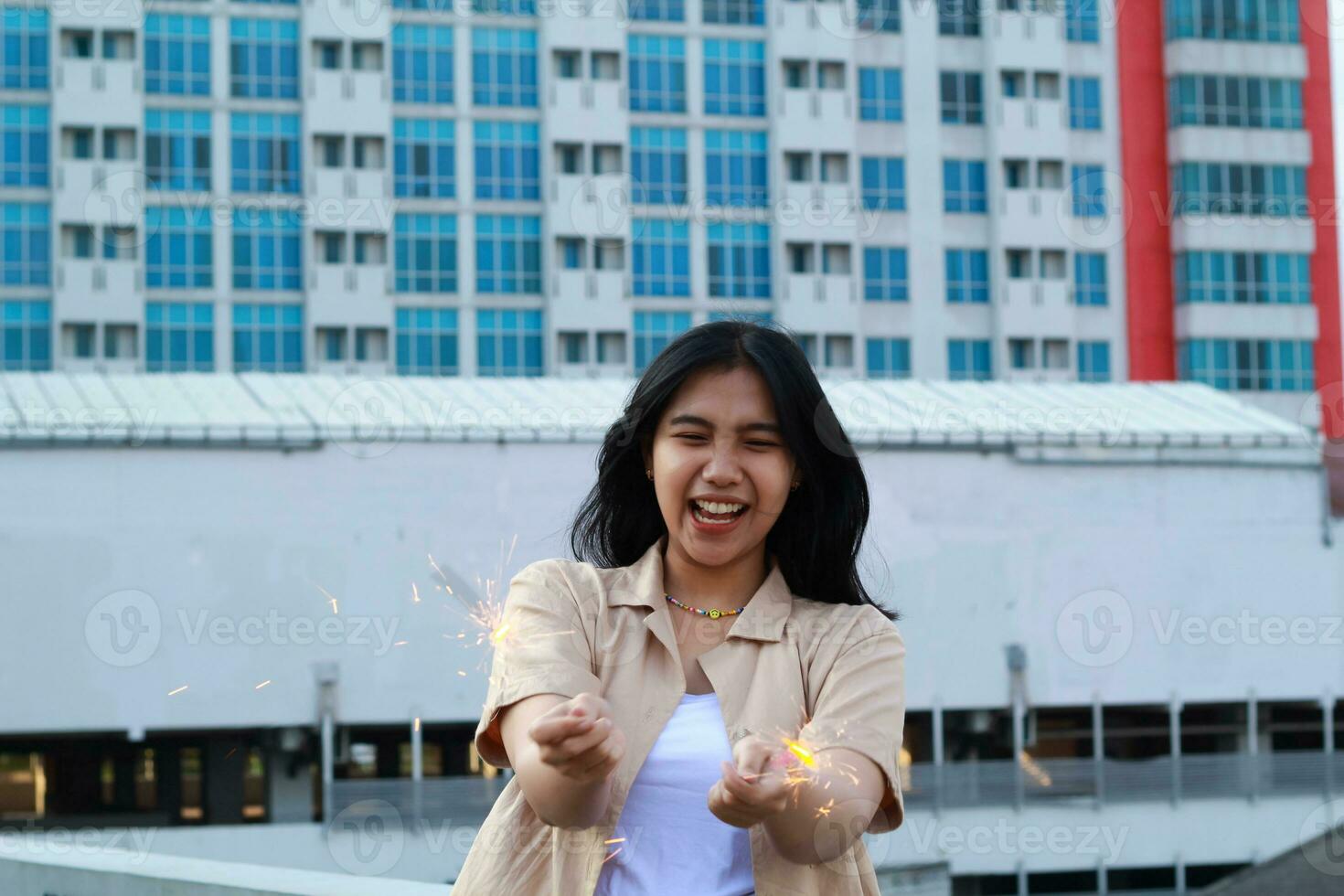 carefree asian young woman holding sparkler celebrate new year eve with laugh and dance in rooftop apartment outdoor with city building background photo