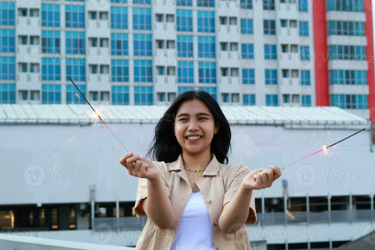 carefree asian young woman holding sparkler celebrate new year eve with laugh and dance in rooftop apartment outdoor with city building background photo