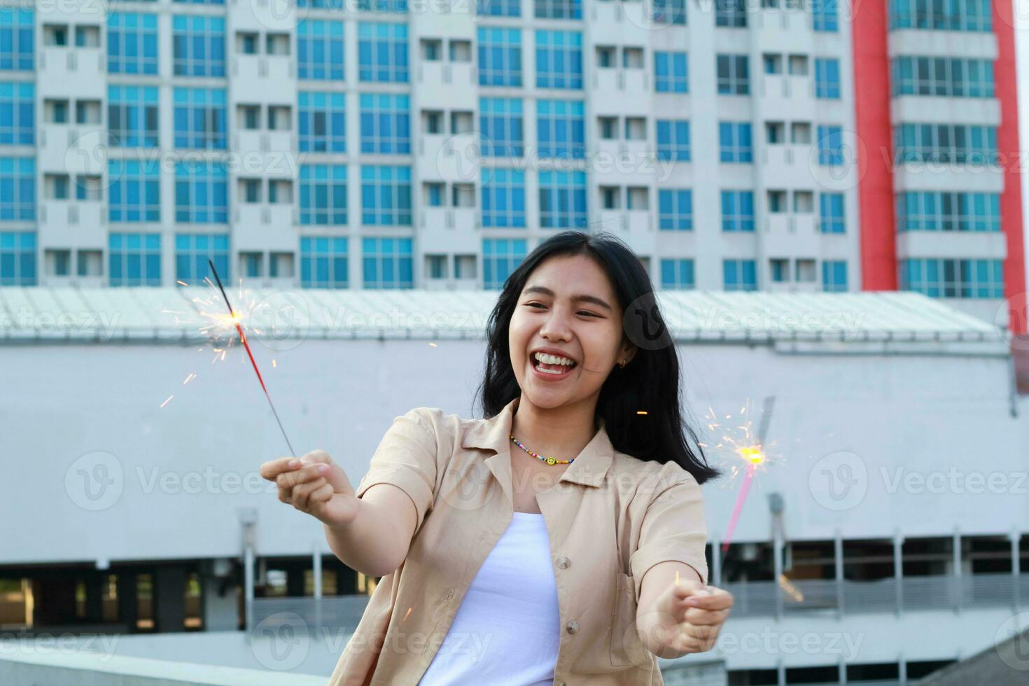 happy asian young woman hipster holding sparklers firework celebrate new year eve with dancing in roof top apartment with urban building background photo