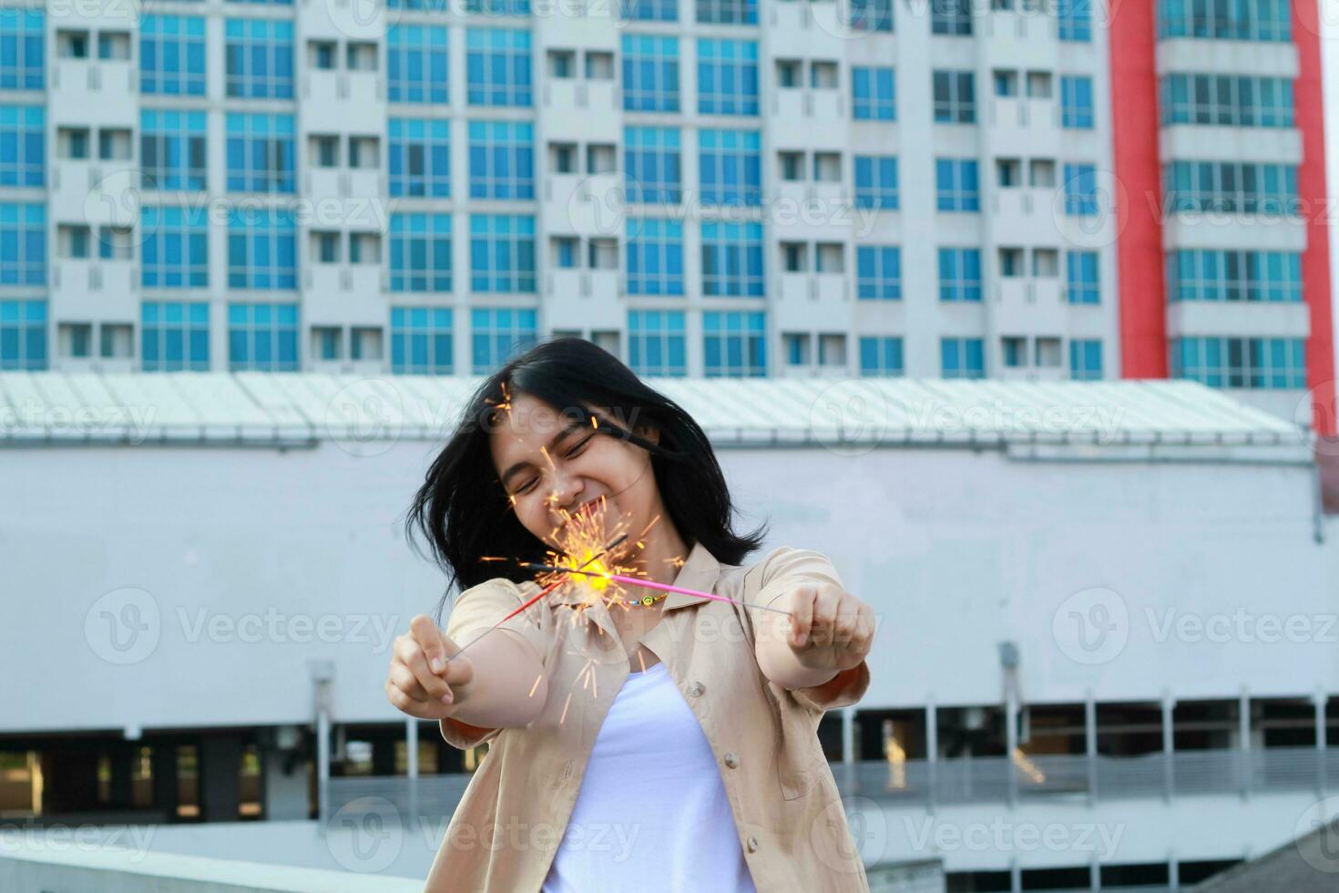 happy asian young woman hipster holding sparklers firework celebrate new year eve with dancing in roof top apartment with urban building background photo