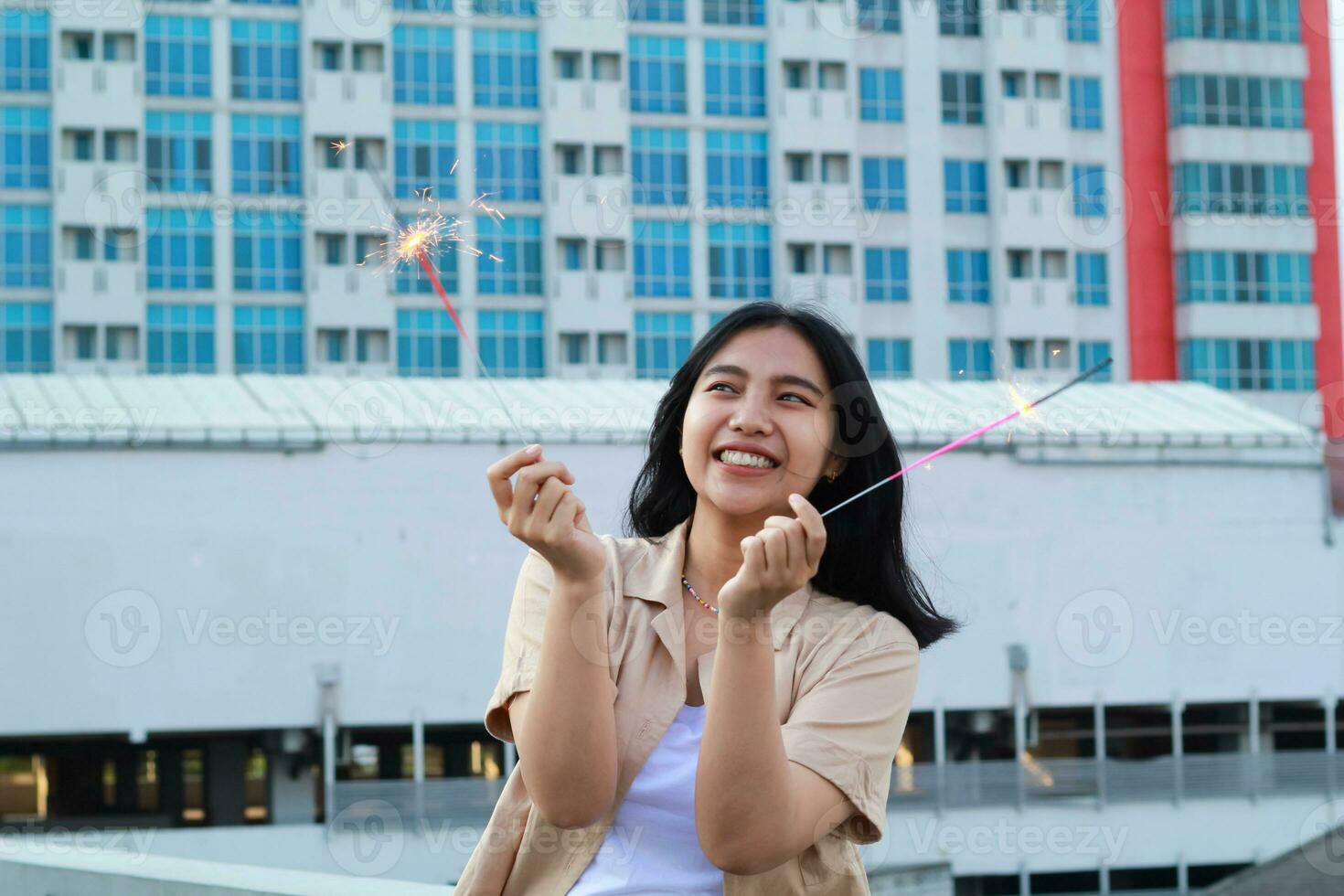 happy asian young woman hipster holding sparklers firework celebrate new year eve with dancing in roof top apartment with urban building background photo