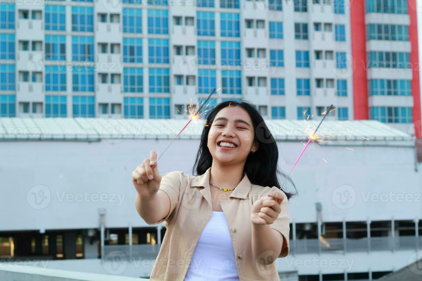 happy asian young woman hipster holding sparklers firework celebrate new year eve with dancing in roof top apartment with urban building background photo