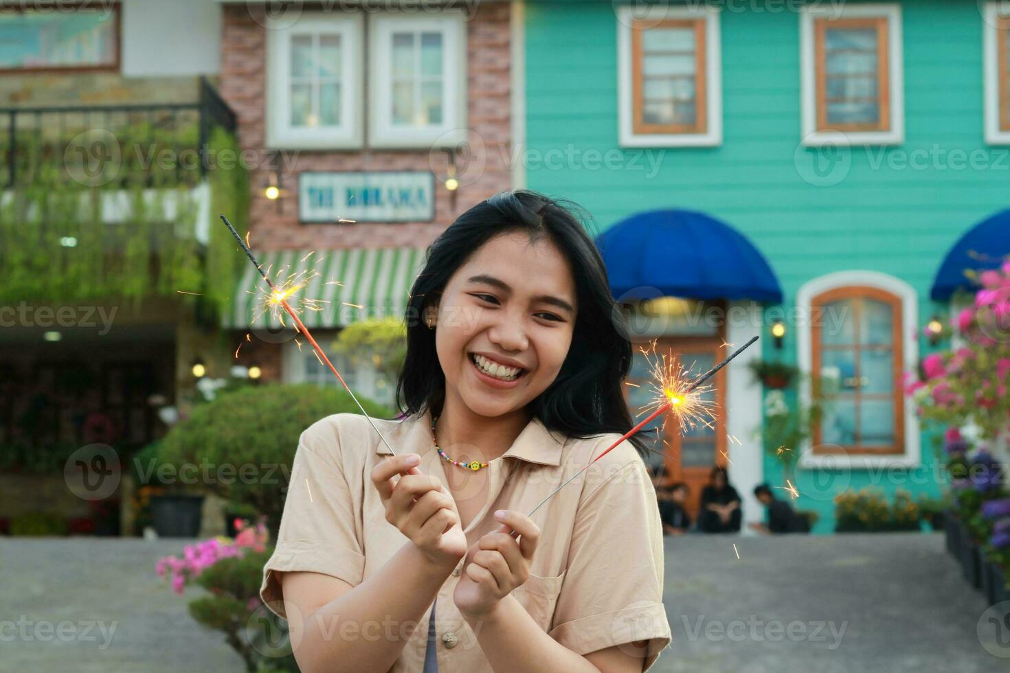 alegre joven asiático mujer participación bengala a celebrar nuevo año víspera con jardín fiesta en pie terminado vistoso Clásico casa yarda foto