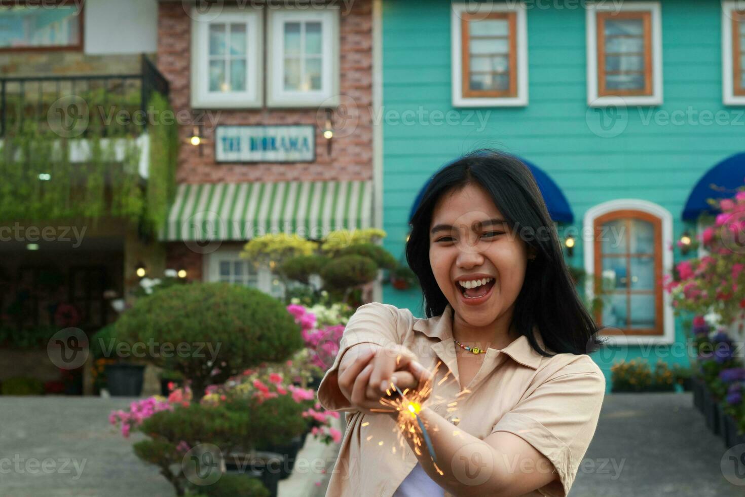 nuevo año víspera celebracion concepto. atractivo asiático joven mujer participación bengala con riendo contento en al aire libre jardín de Clásico casa yarda foto