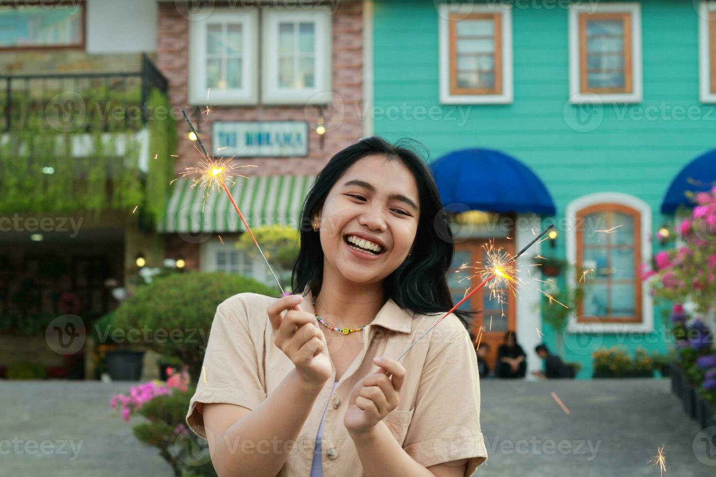 cheerful young asian woman holding sparkler to celebrate new year eve with garden party standing over colorful vintage house yard photo