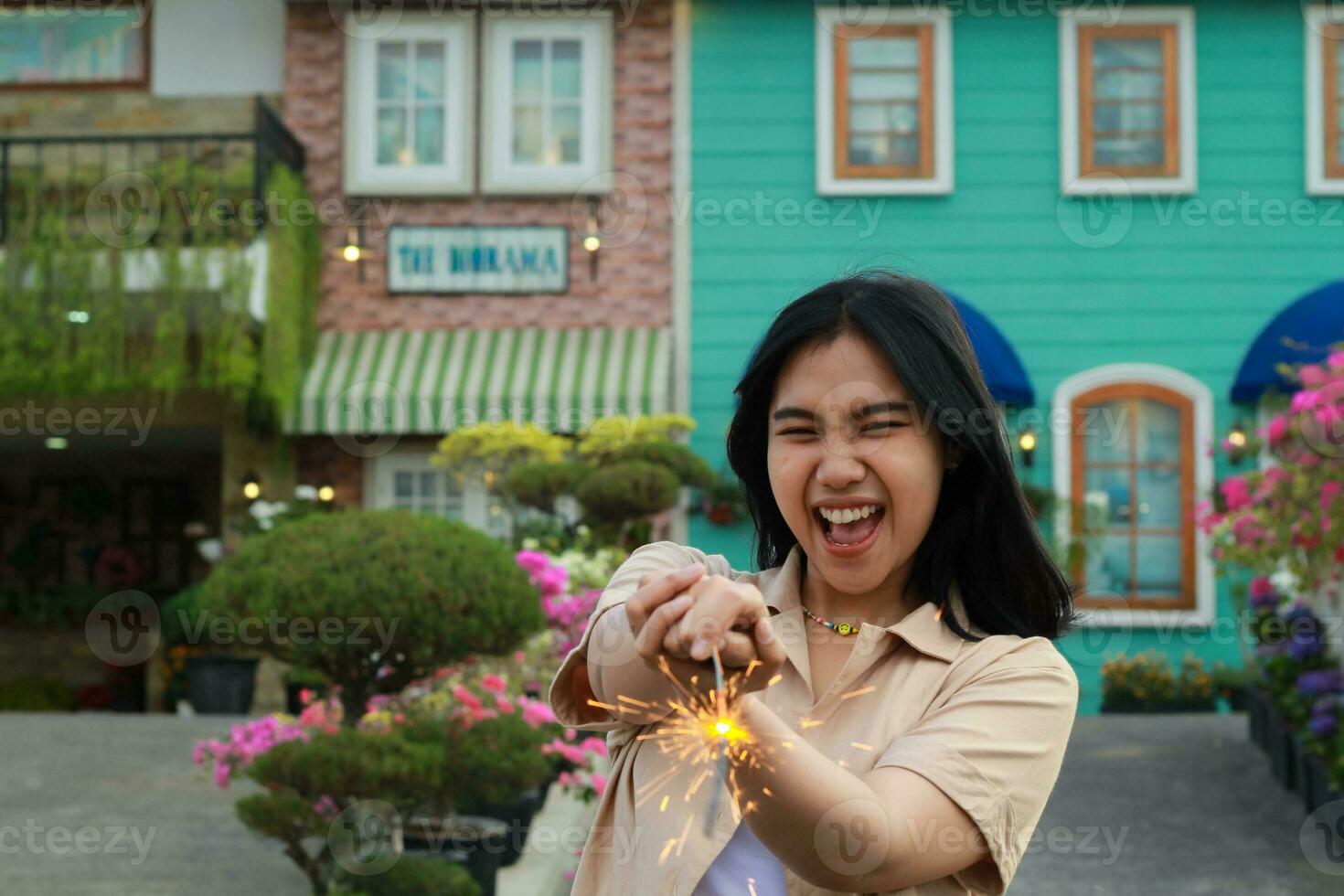 nuevo año víspera celebracion concepto. atractivo asiático joven mujer participación bengala con riendo contento en al aire libre jardín de Clásico casa yarda foto