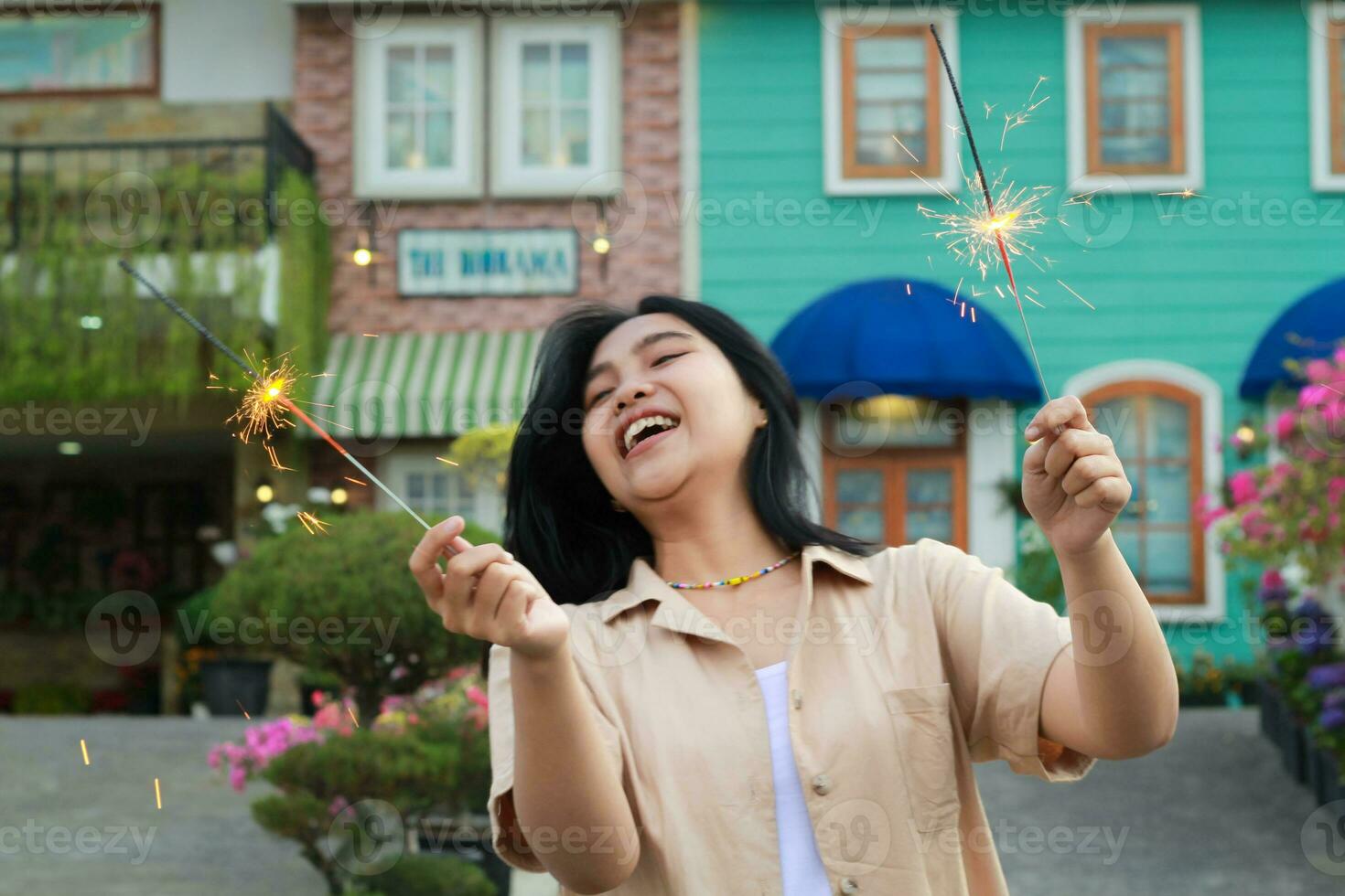 retrato de hermosa contento joven asiático mujer participación bengalas fuegos artificiales a celebrar nuevo año víspera con jardín fiesta en pie en al aire libre Clásico casa yarda foto