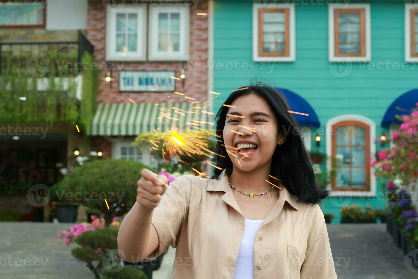 portrait of beautiful happy young asian woman holding sparklers fireworks to celebrate new year eve with garden party standing in outdoor vintage house yard photo