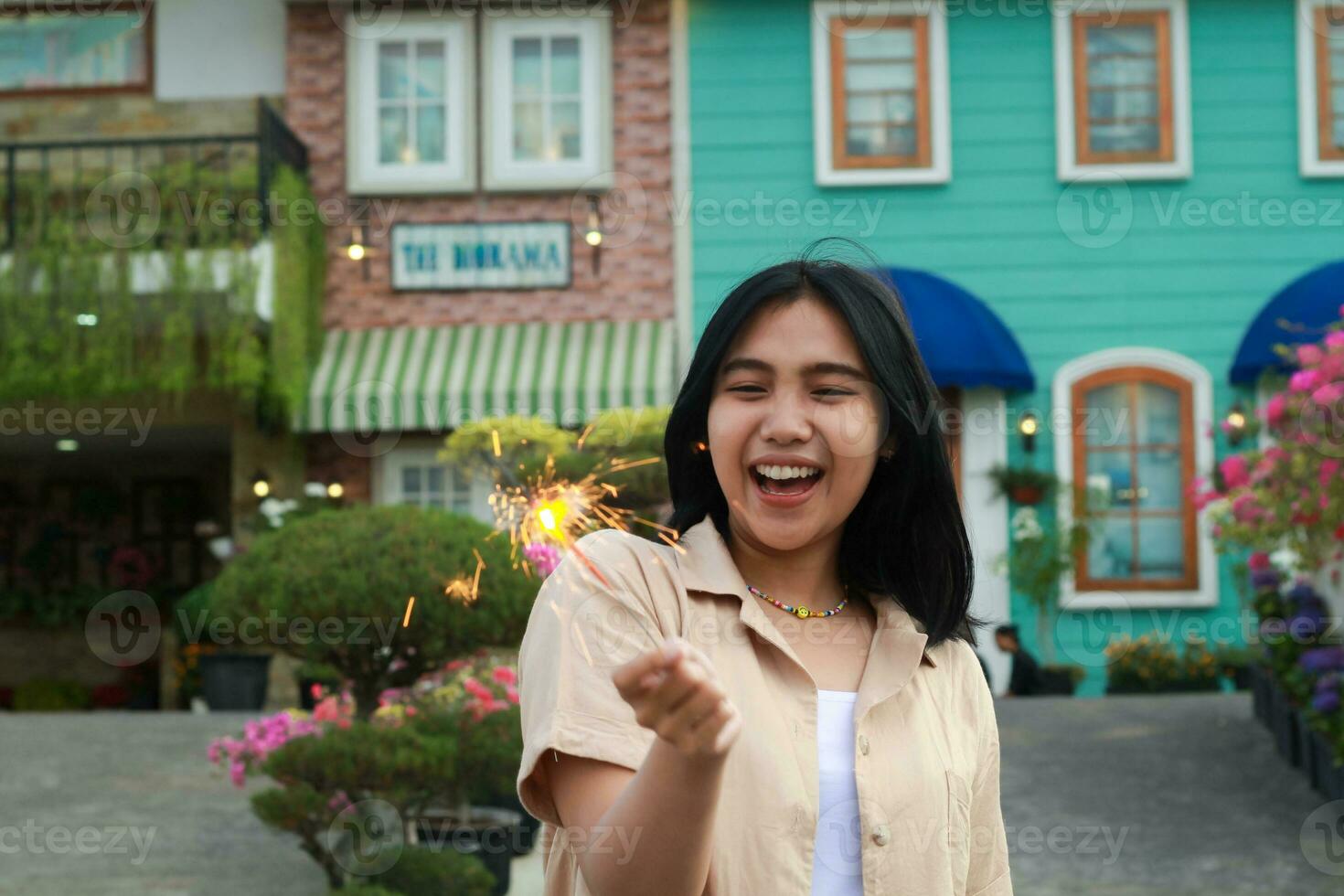 portrait of beautiful happy young asian woman holding sparklers fireworks to celebrate new year eve with garden party standing in outdoor vintage house yard photo