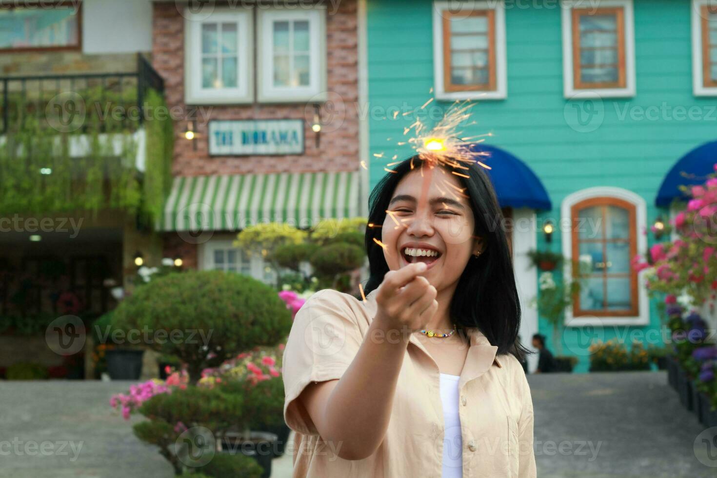 portrait of beautiful happy young asian woman holding sparklers fireworks to celebrate new year eve with garden party standing in outdoor vintage house yard photo