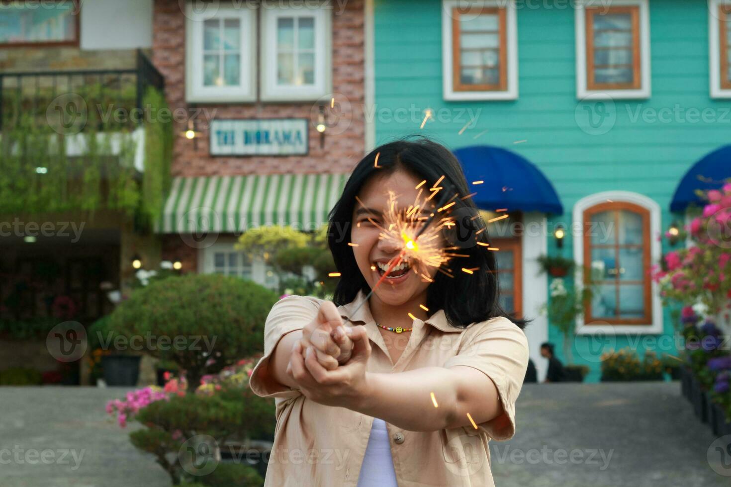 nuevo año víspera celebracion concepto. atractivo asiático joven mujer participación bengala con riendo contento en al aire libre jardín de Clásico casa yarda foto