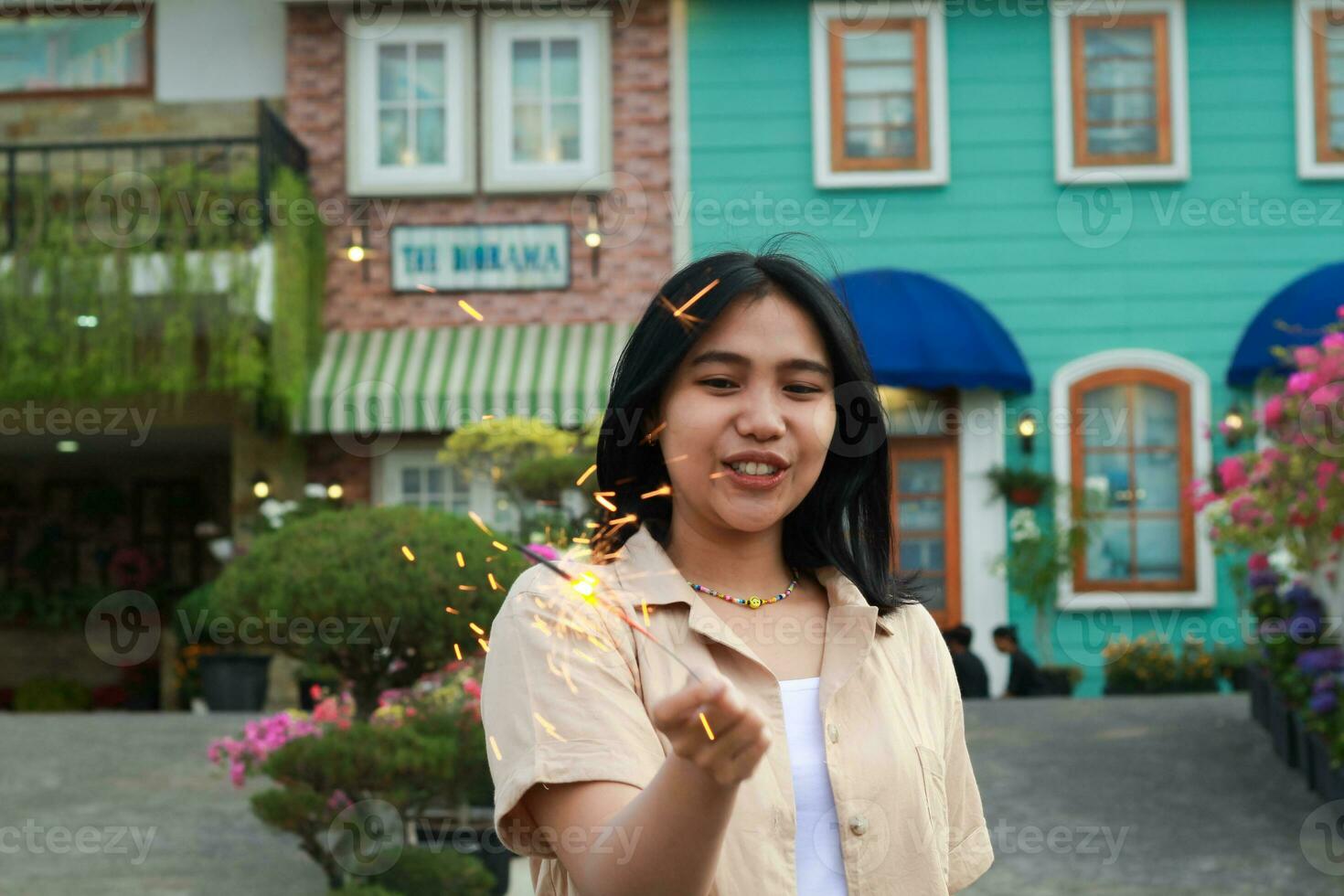 portrait of beautiful happy young asian woman holding sparklers fireworks to celebrate new year eve with garden party standing in outdoor vintage house yard photo