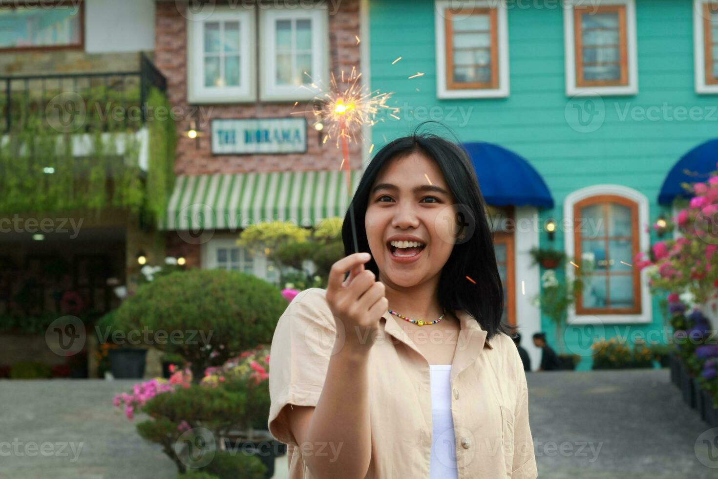 portrait of beautiful happy young asian woman holding sparklers fireworks to celebrate new year eve with garden party standing in outdoor vintage house yard photo