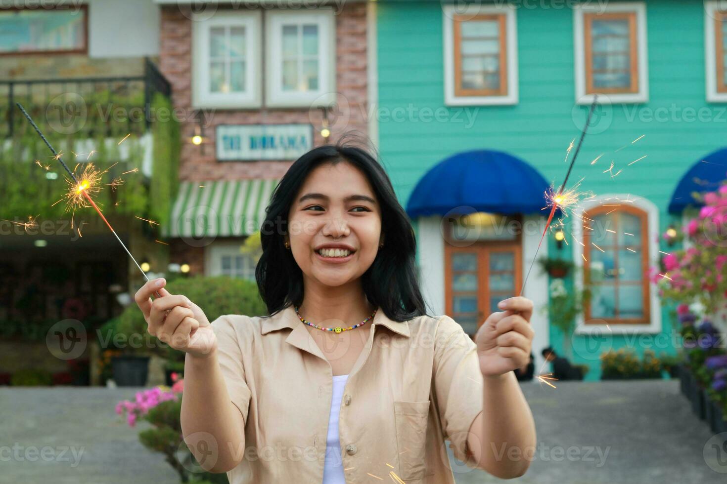 retrato de hermosa contento joven asiático mujer participación bengalas fuegos artificiales a celebrar nuevo año víspera con jardín fiesta en pie en al aire libre Clásico casa yarda foto