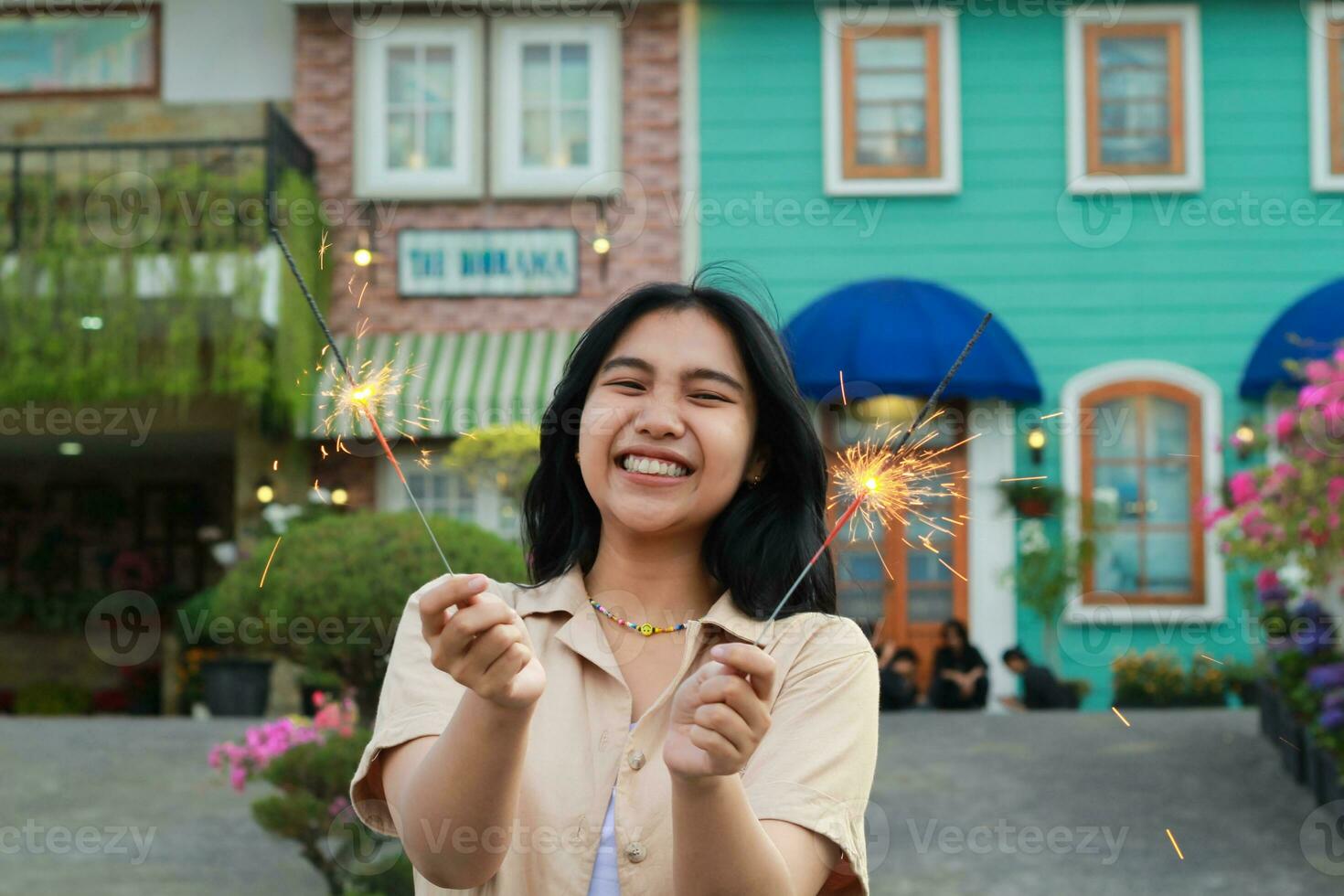portrait of beautiful happy young asian woman holding sparklers fireworks to celebrate new year eve with garden party standing in outdoor vintage house yard photo