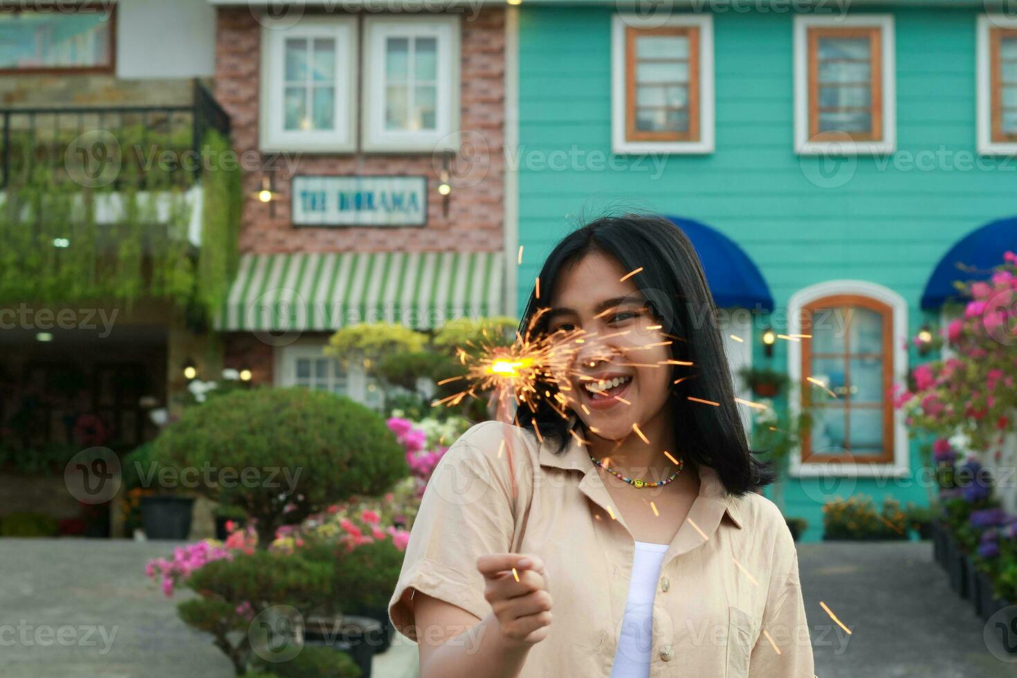 portrait of beautiful happy young asian woman holding sparklers fireworks to celebrate new year eve with garden party standing in outdoor vintage house yard photo