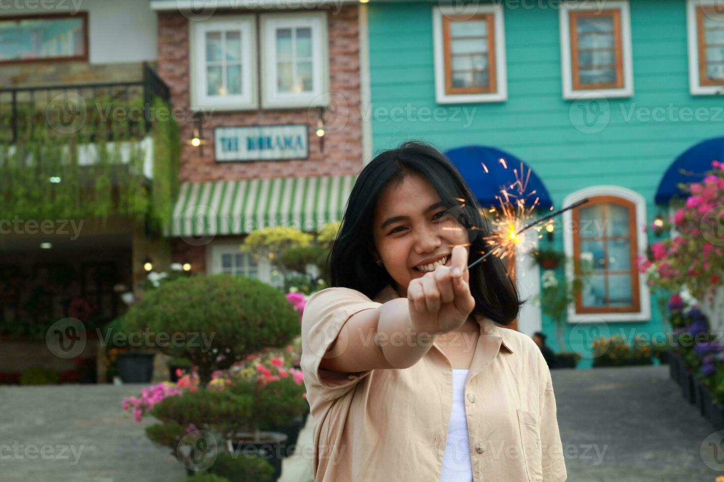 happy young asian woman holding sparkler enjoy new year eve celebration in outdoor garden of colorful vintage house in evening photo