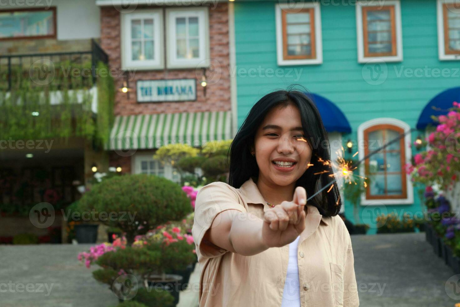 happy young asian woman holding sparkler enjoy new year eve celebration in outdoor garden of colorful vintage house in evening photo