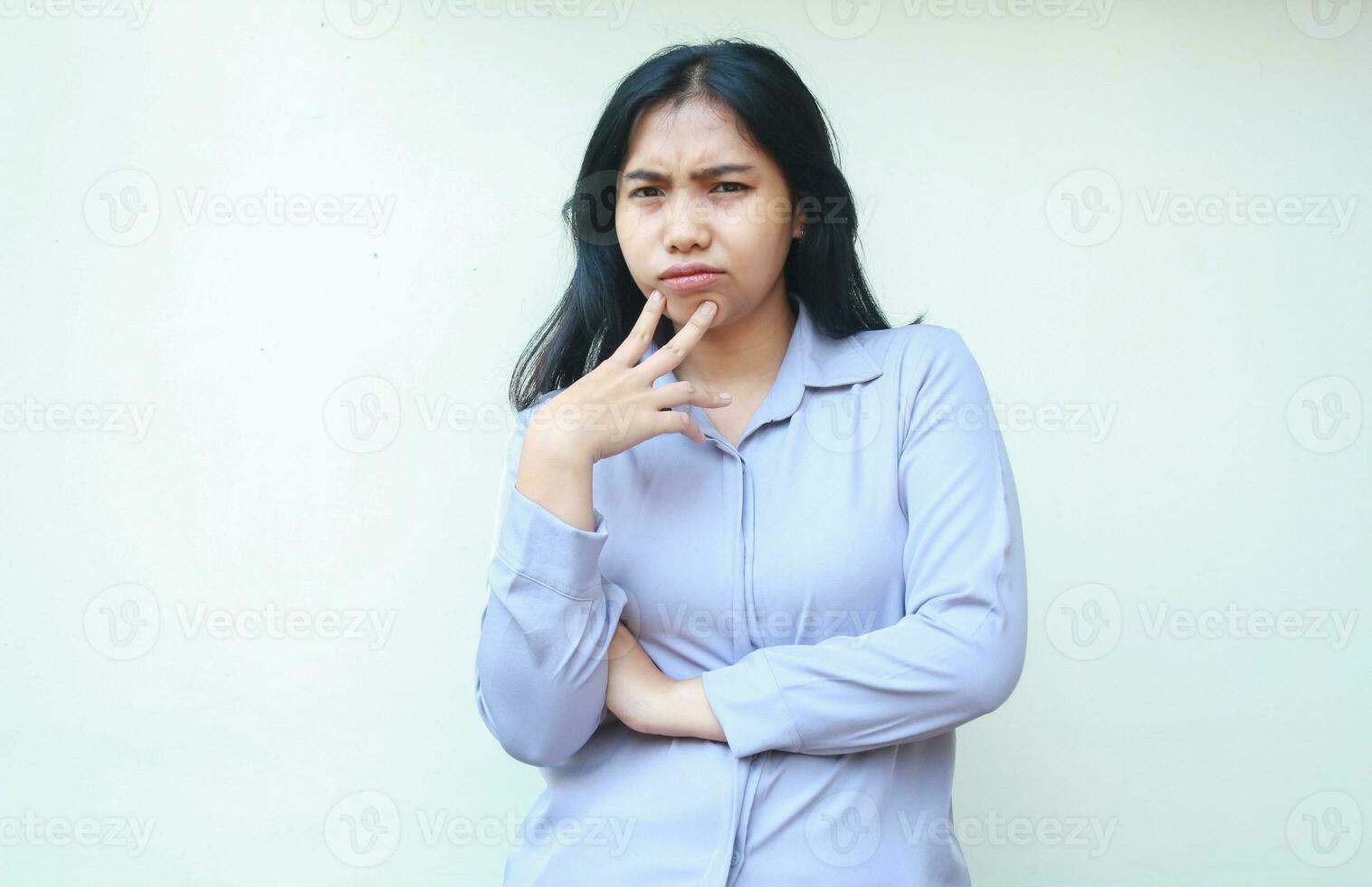 thoughful serious asian young woman employee looking to camera suspiciously with folded arm and touching chin isolated on white background photo