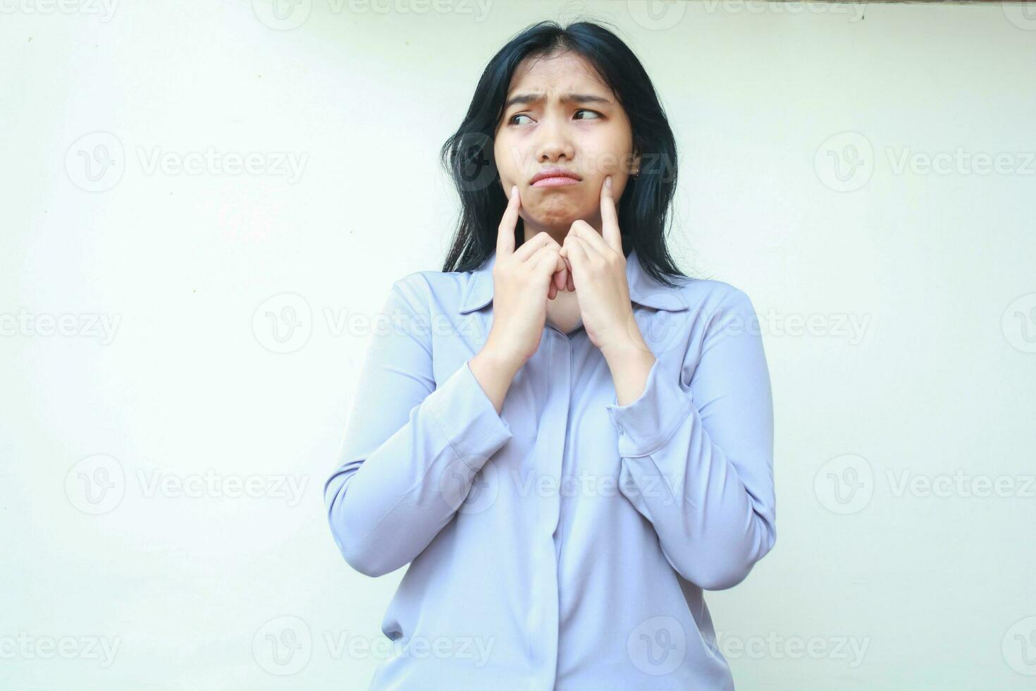 sad worried asian young woman looking away with thoughtful expression and thouching her cheek with forefinger isolated over white background photo