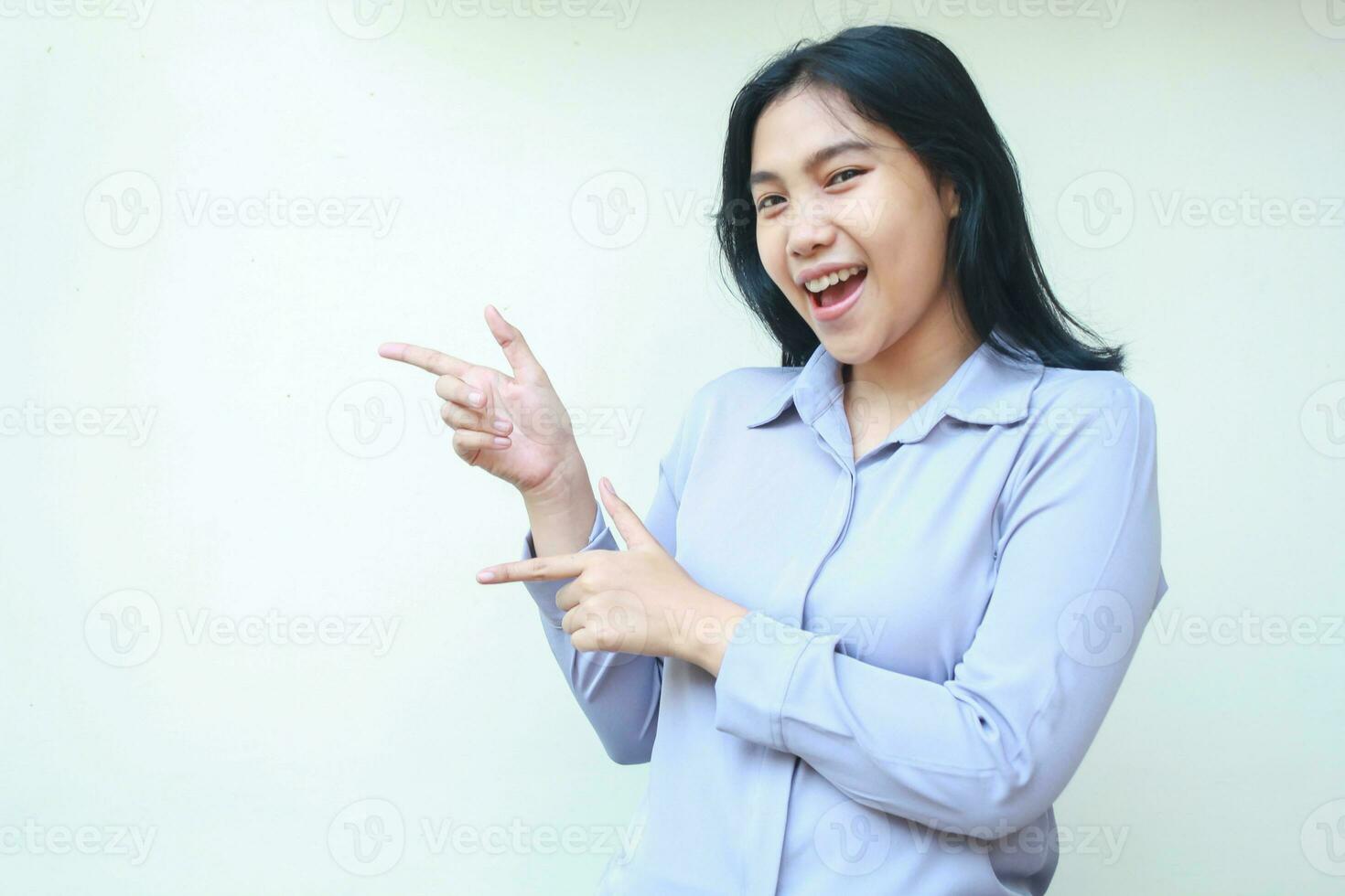 presenting asian young woman pointing finger to side looking to camera smiling with excitement, wearing formal shirt isolated on white background photo