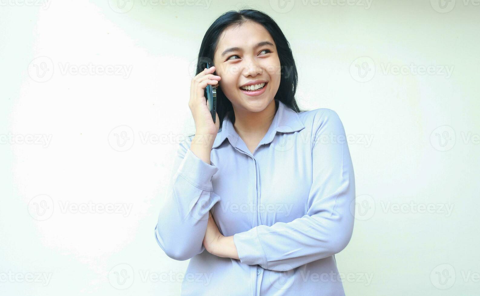 smiling asian young business woman excited to make a call to talking on cell phone looking away with folded arm wear formal shirt isolated on white background photo